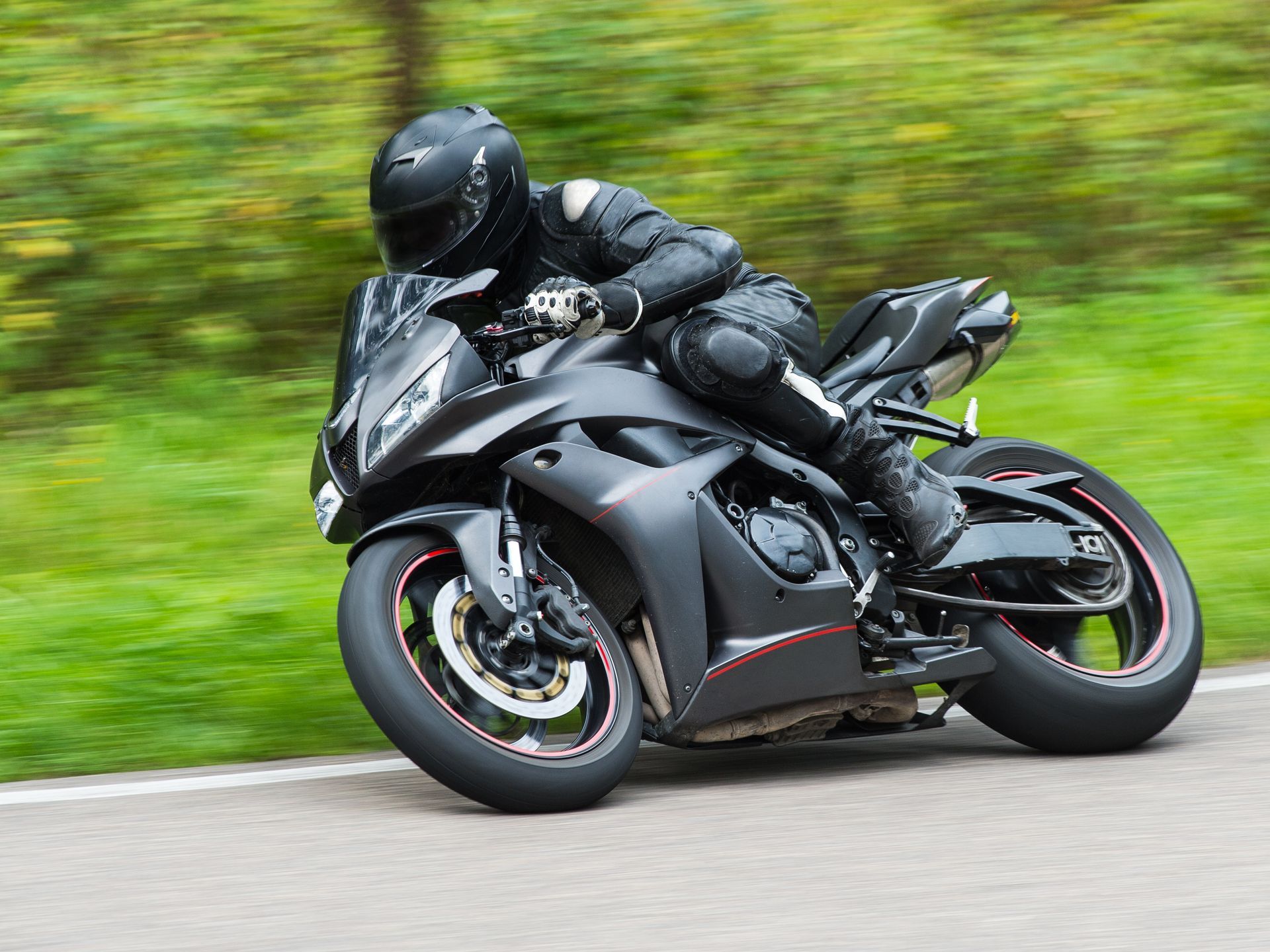 A man is riding a black motorcycle down a road.