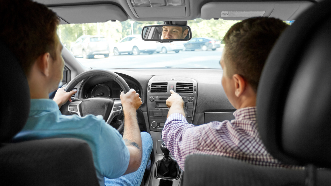A man is teaching another man how to drive a car.