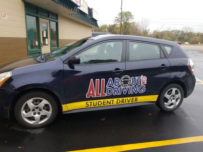 A blue all about driving student driver car is parked in a parking lot