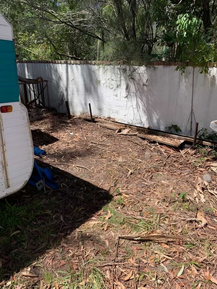 A White Trailer is Parked in a Yard Next to a White Wall — A Load of Rubbish In Nambour, QLD