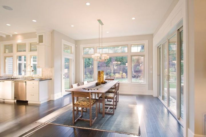 Dining room with a long wooden table, chairs, and large windows overlooking a yard.