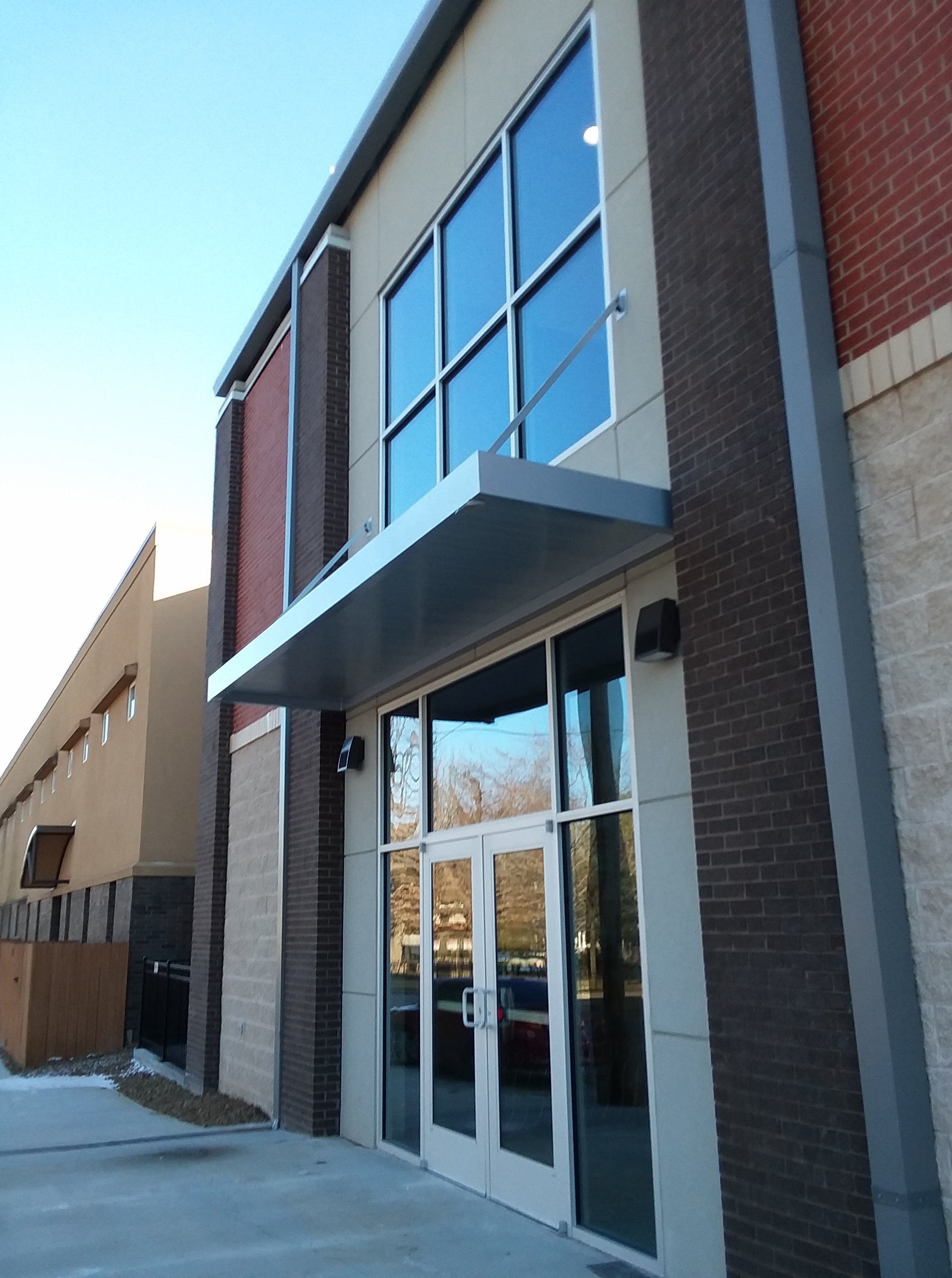 Exterior of a modern building with large windows, glass doors, brick accents, and a metal awning.