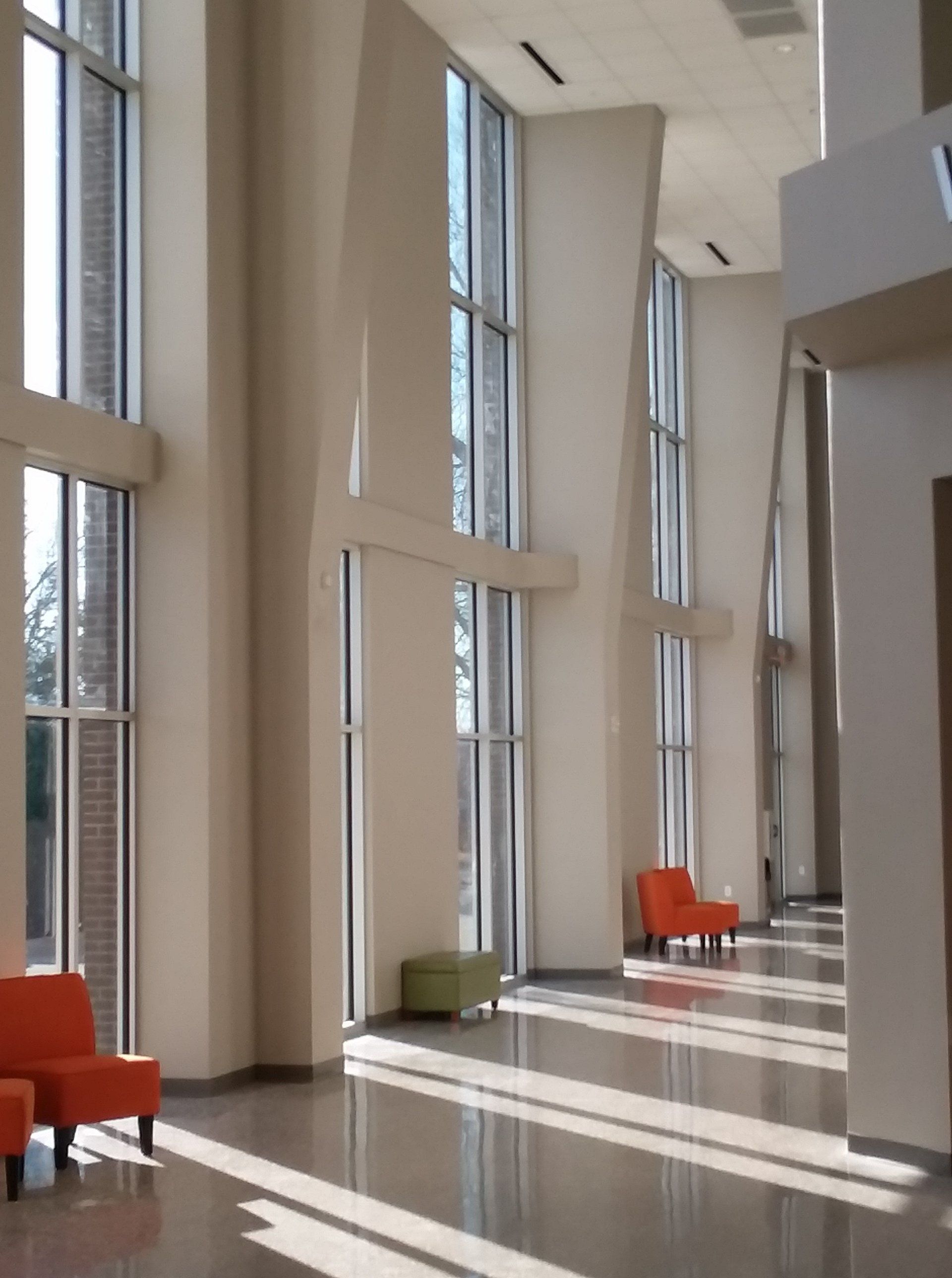 Interior view of a modern lobby with large windows, orange chairs, and shiny floor.