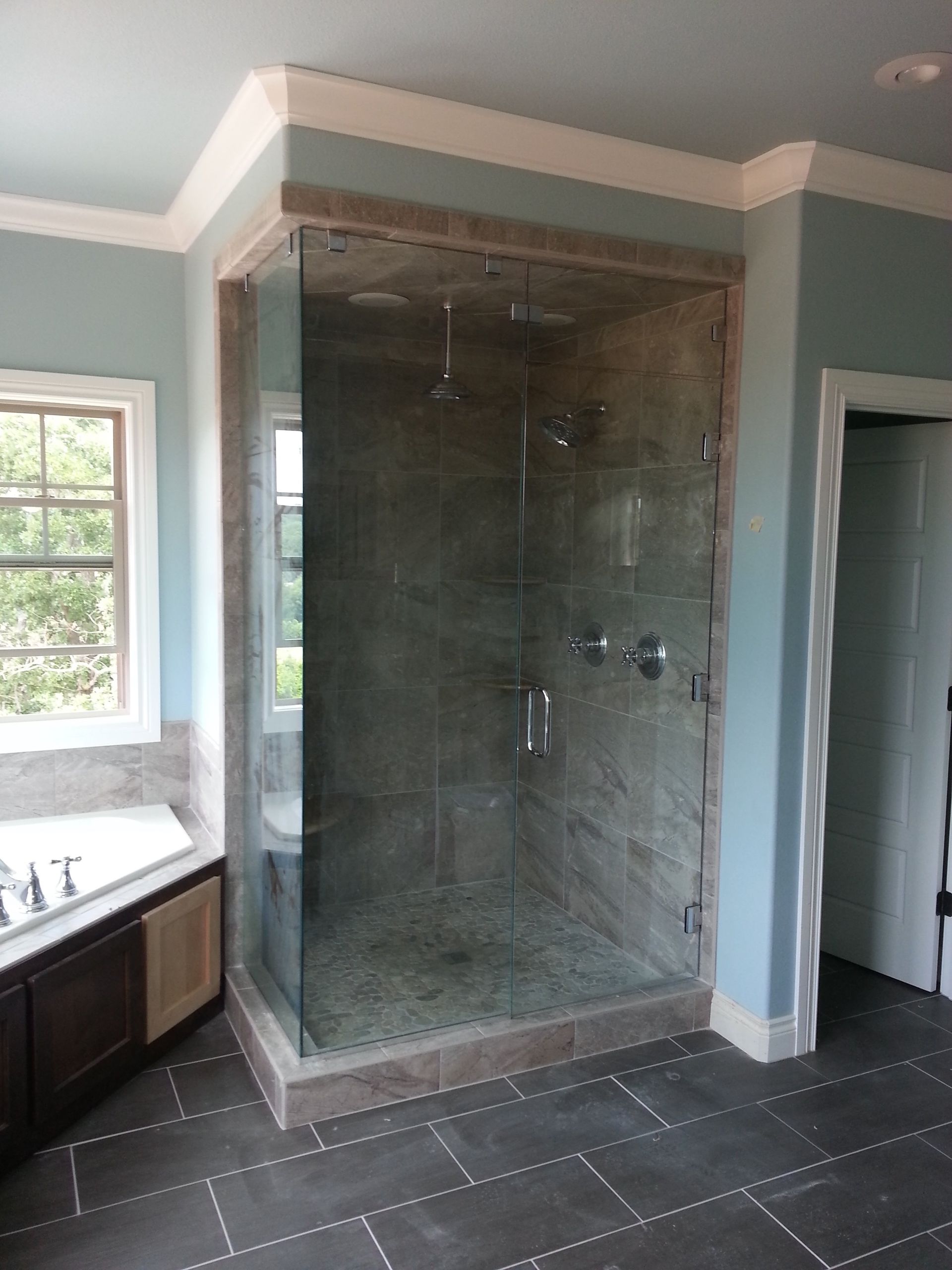 Glass shower enclosure in a blue-walled bathroom with stone tiles and a view of the outdoors.