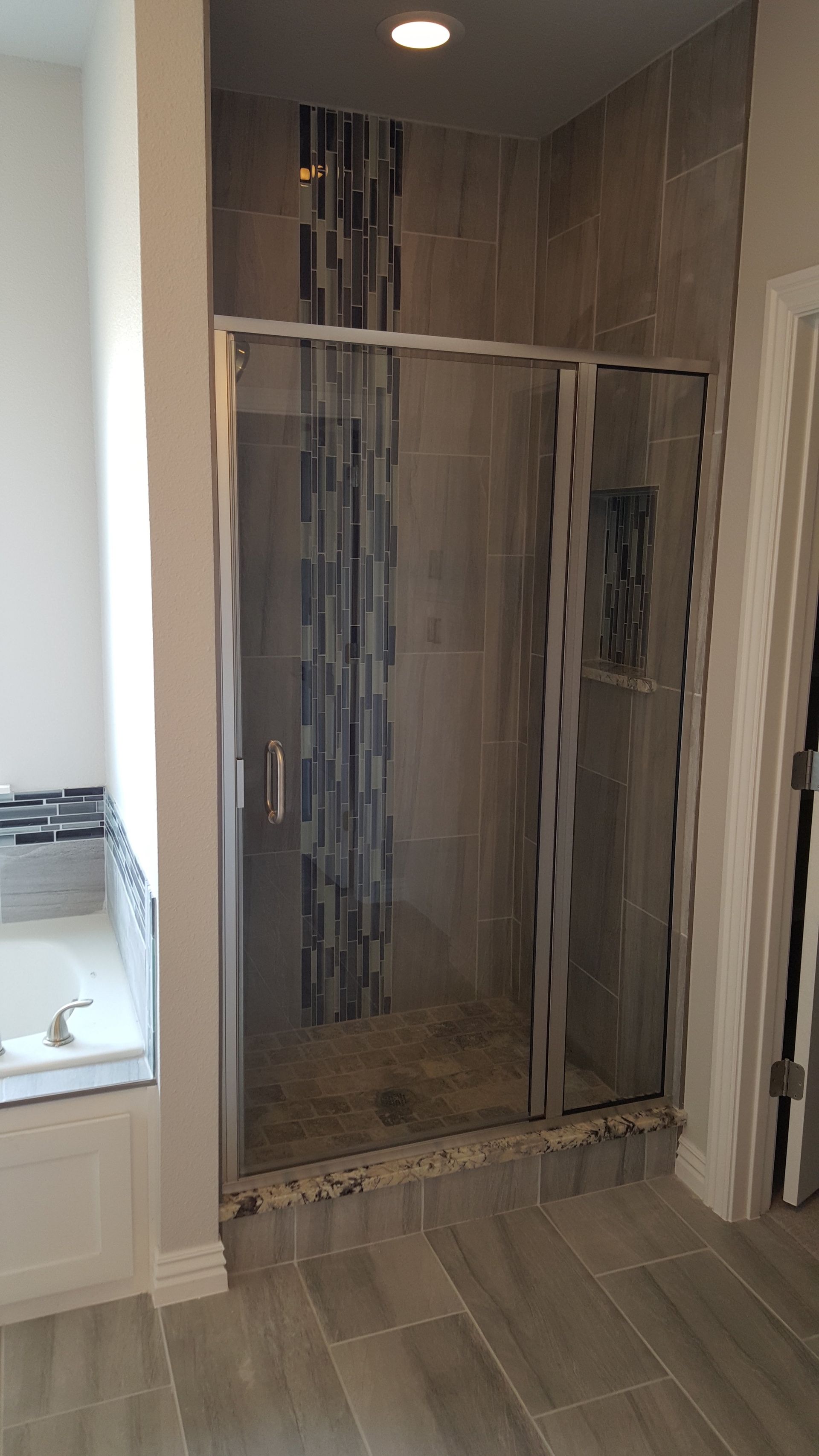 Shower with glass door and tiled walls, featuring a mosaic accent.