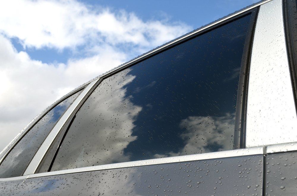 Car window reflecting a cloudy sky; silver trim and dark tint.