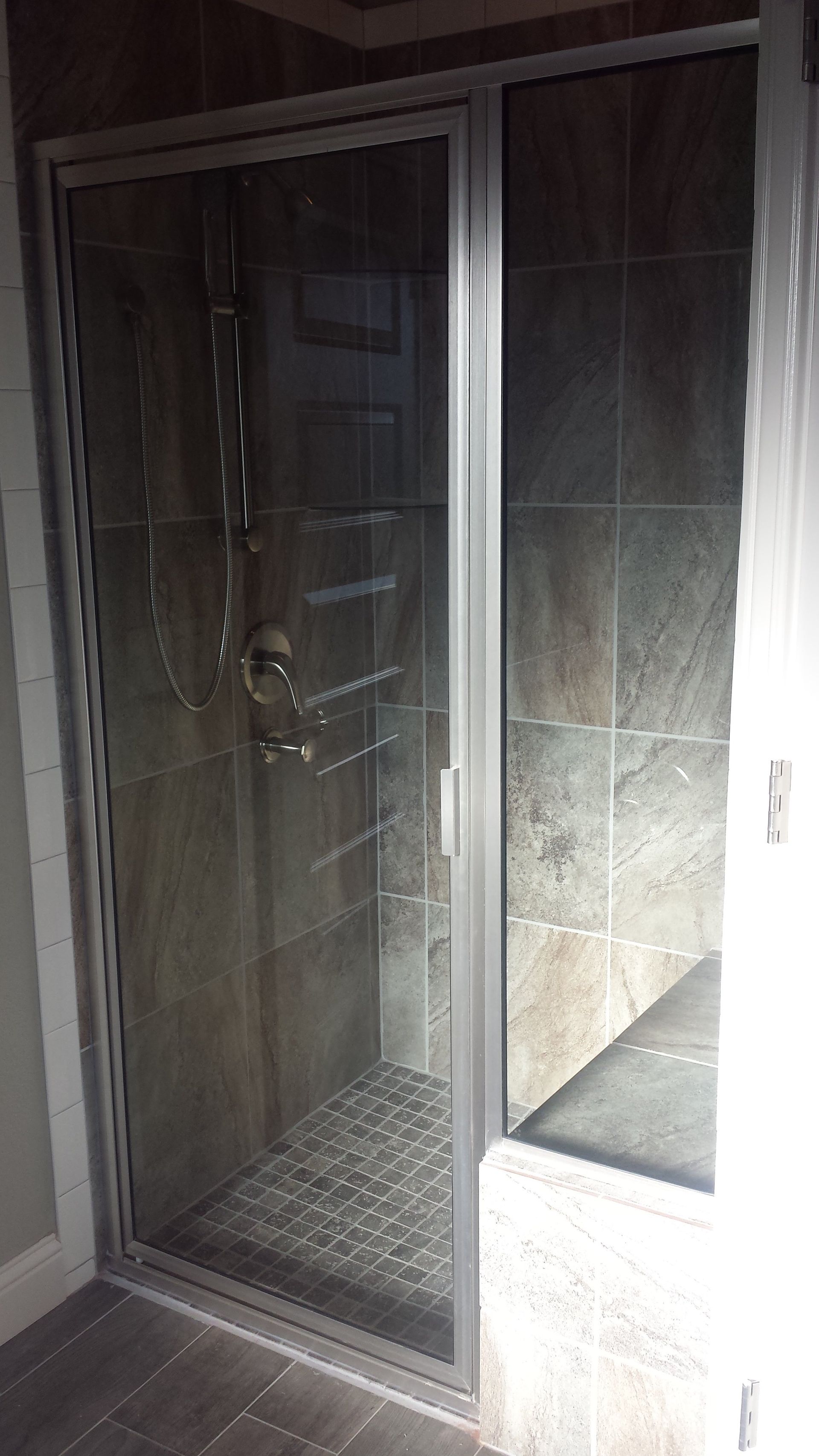 Shower stall with glass door, gray tile, and pebble floor.