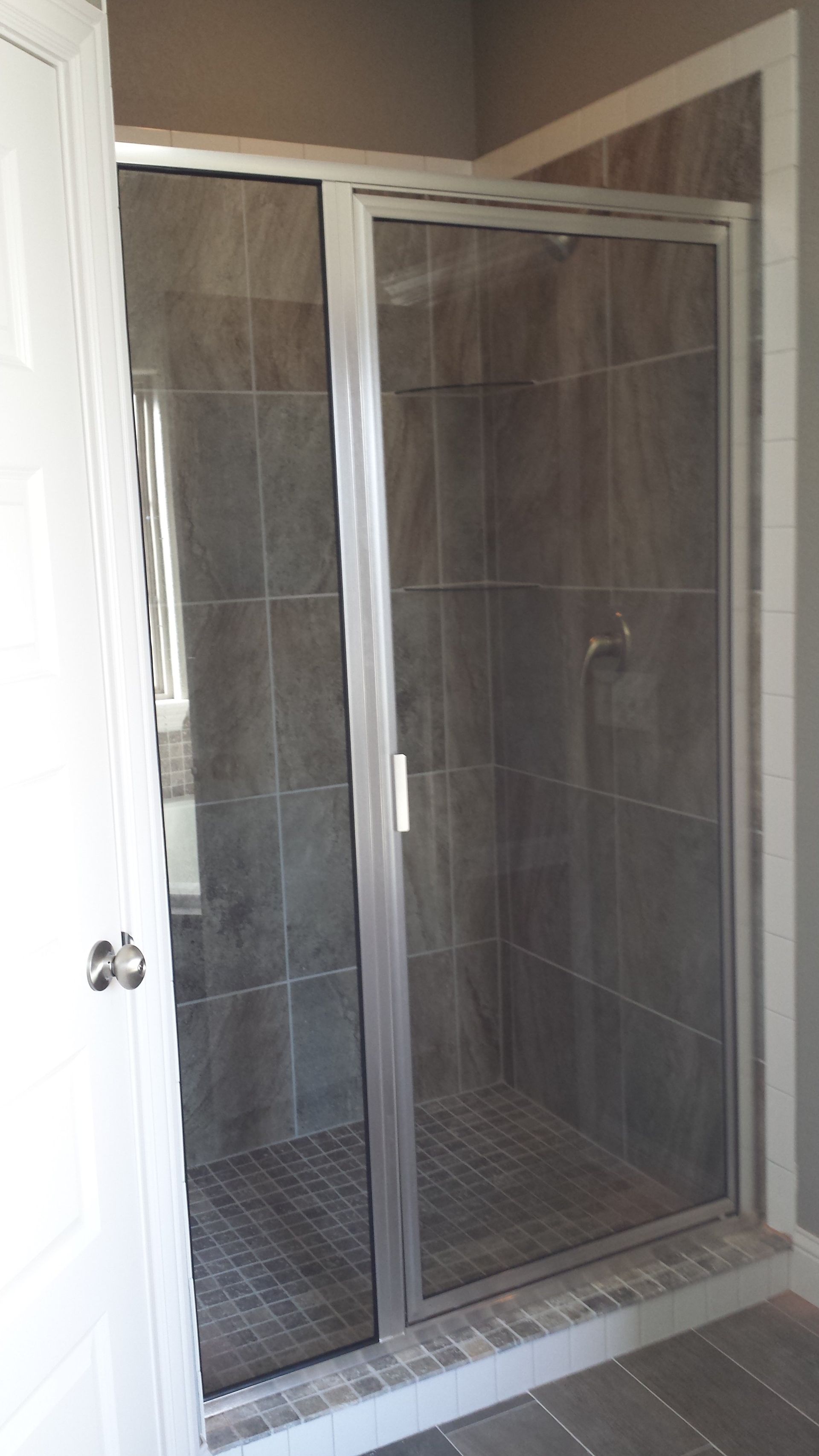 A shower enclosure with a sliding glass door, gray tiles, and a silver frame.