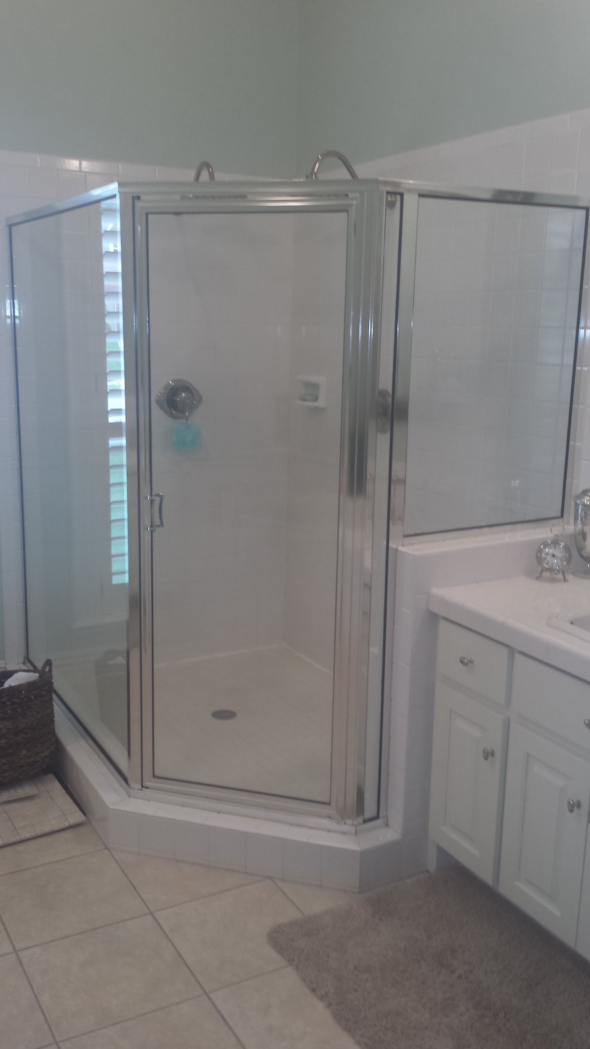 Corner glass shower in a bathroom with white cabinetry and light tile.