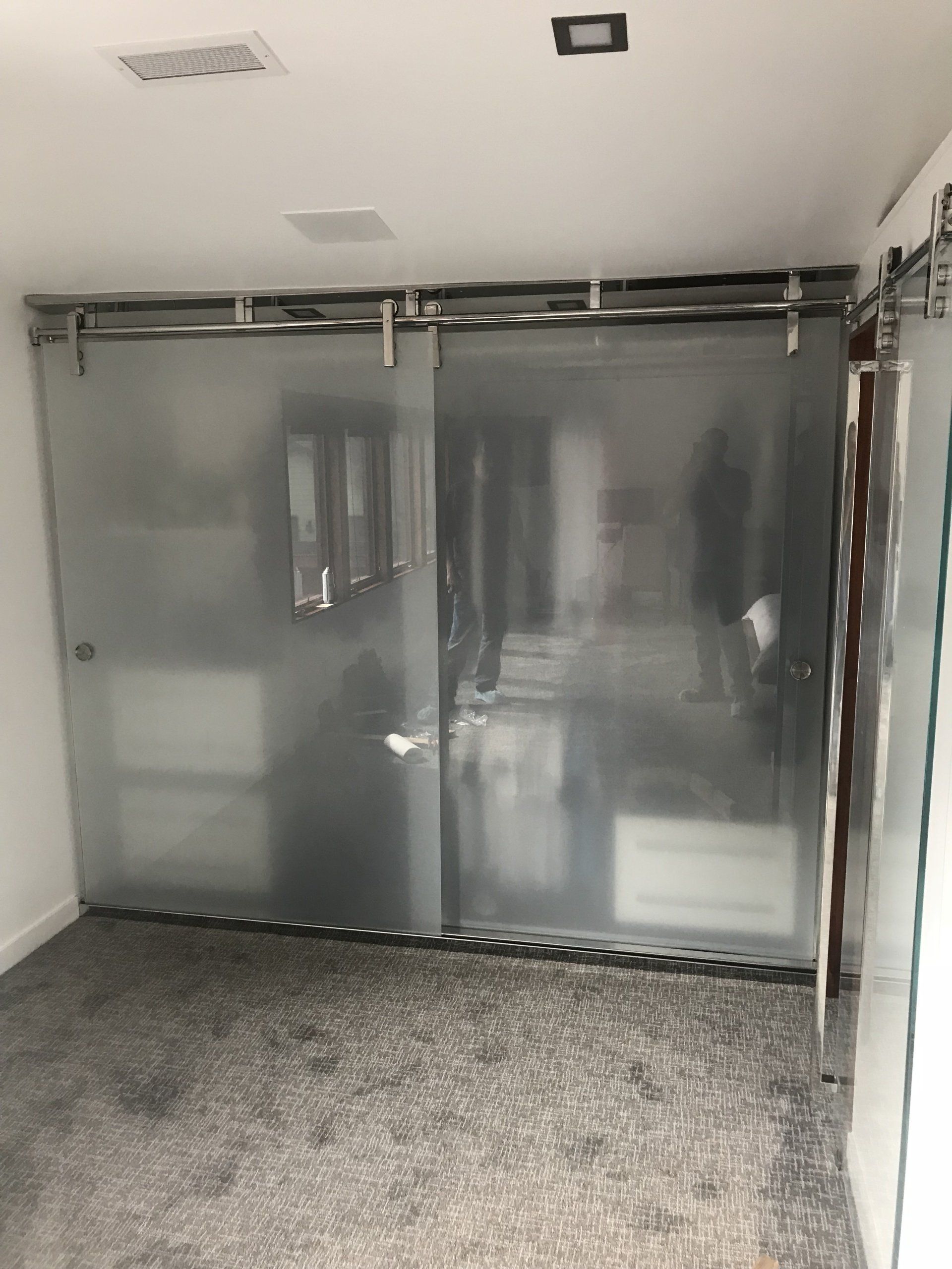 Frosted glass sliding doors on a track, indoors.  Silver hardware, gray carpet, white walls, square light fixture.