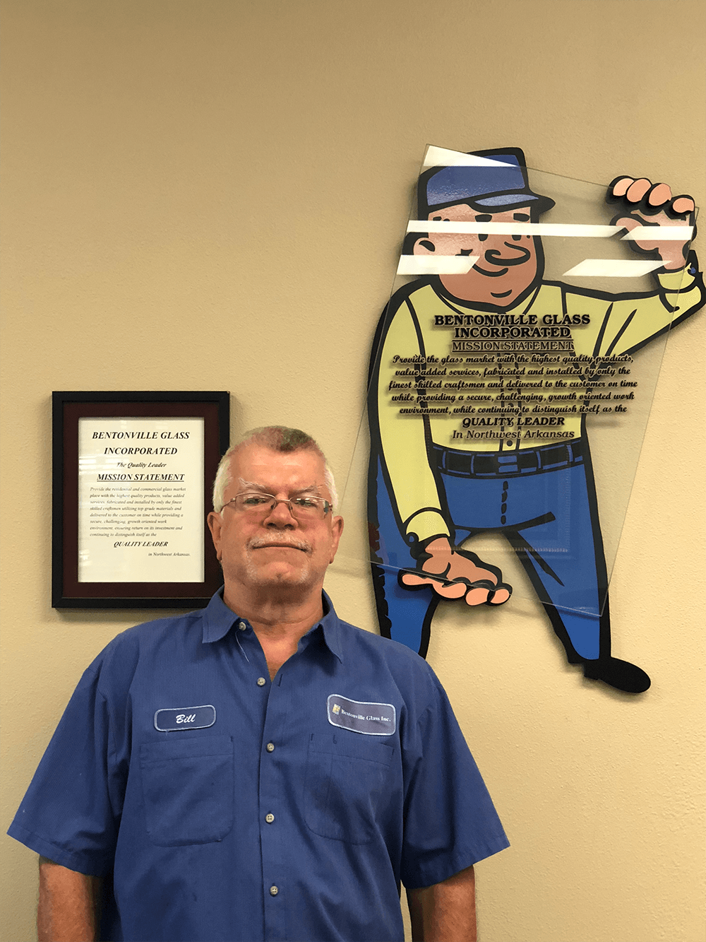 Man in blue shirt stands next to a cartoon sign of a worker. Award on the wall.