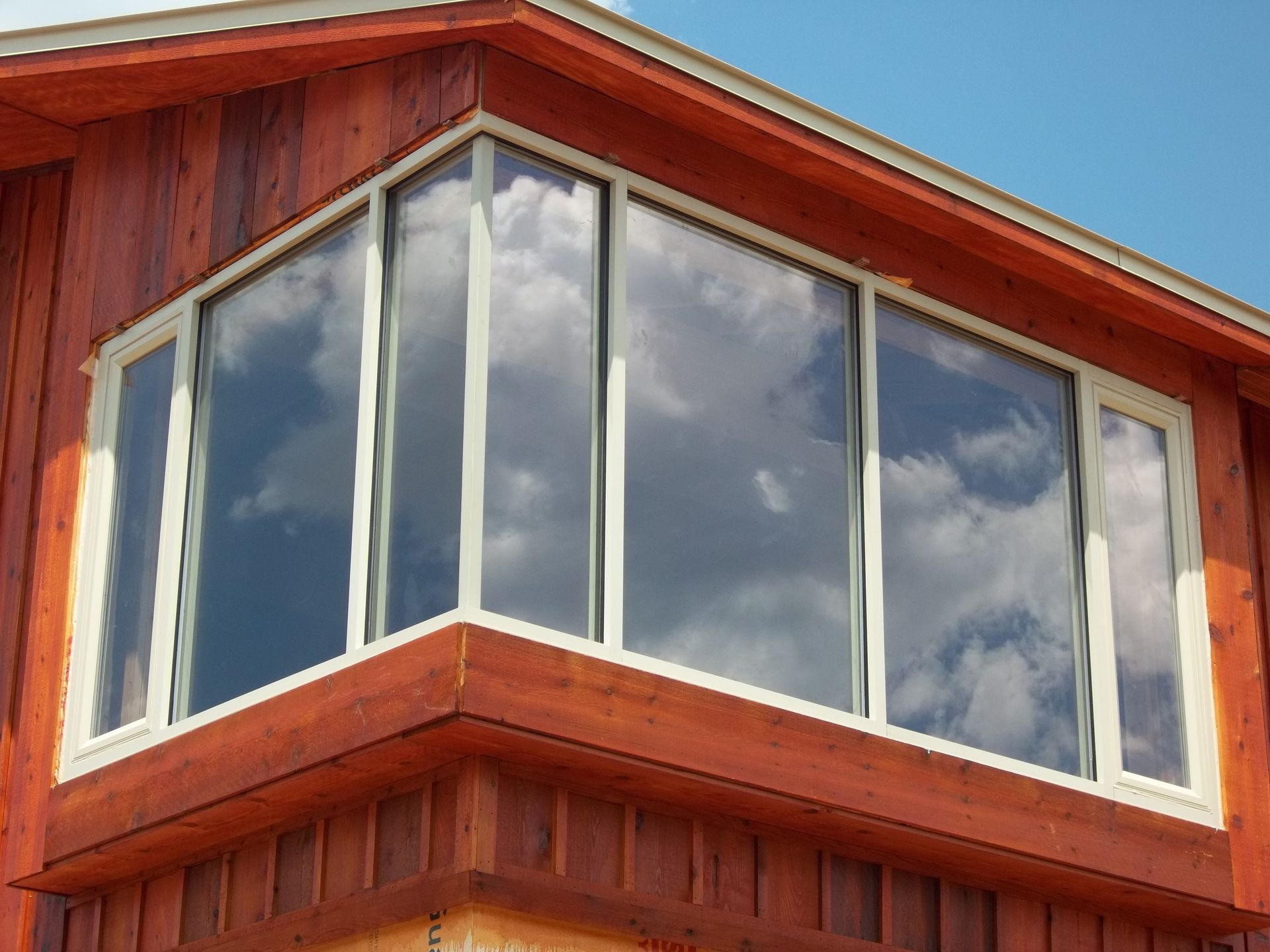 Large windows on a wooden building reflect the sky with clouds.