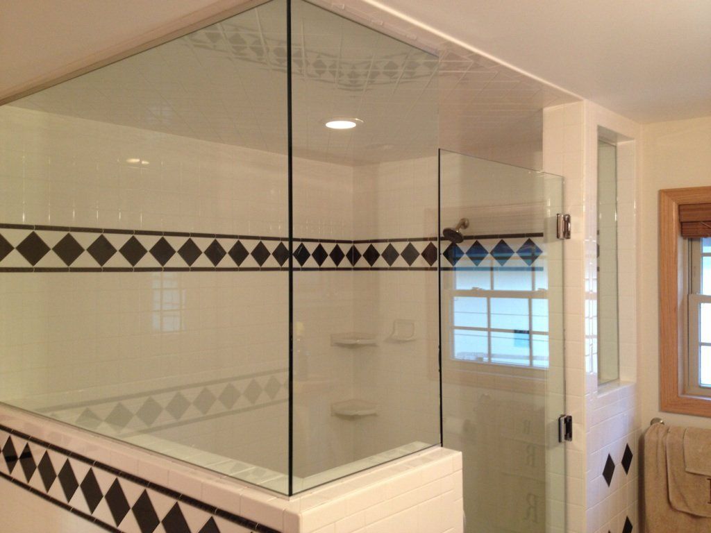 Glass-walled shower with white and black tiled walls and a window, bathroom.