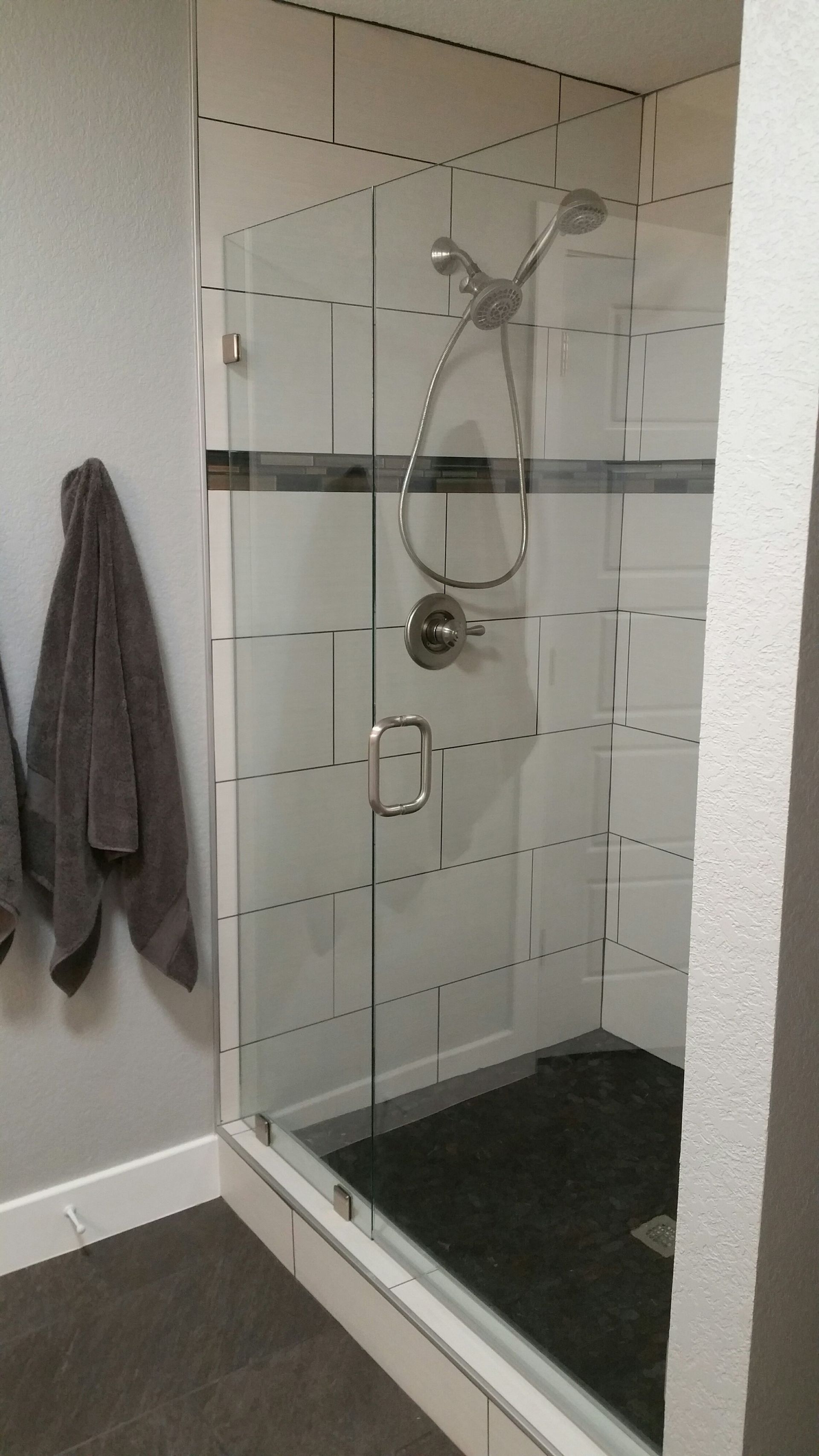 A glass shower with white subway tiles, gray floor, and a silver showerhead.