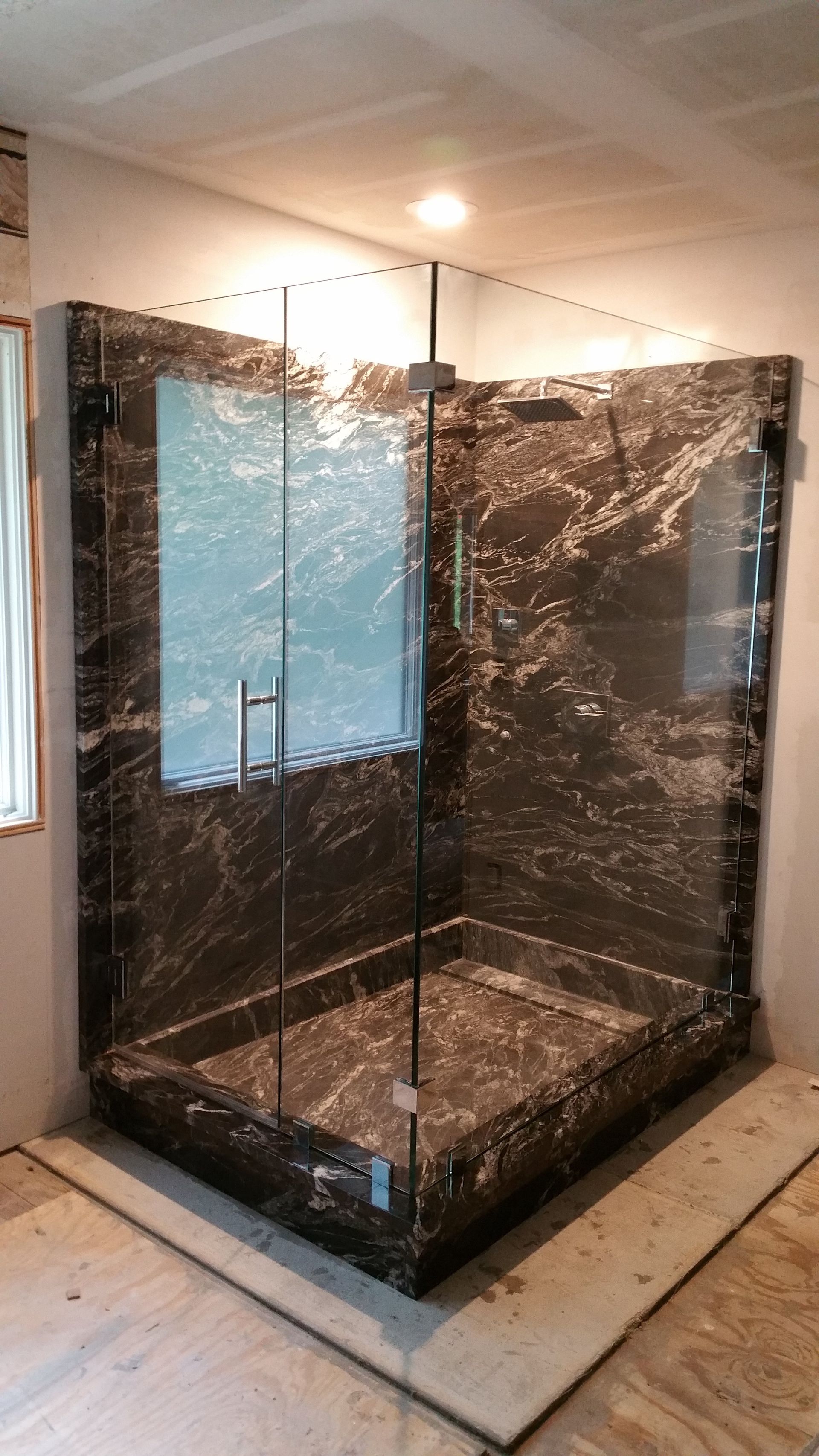 Corner shower with dark marbled walls and glass doors.