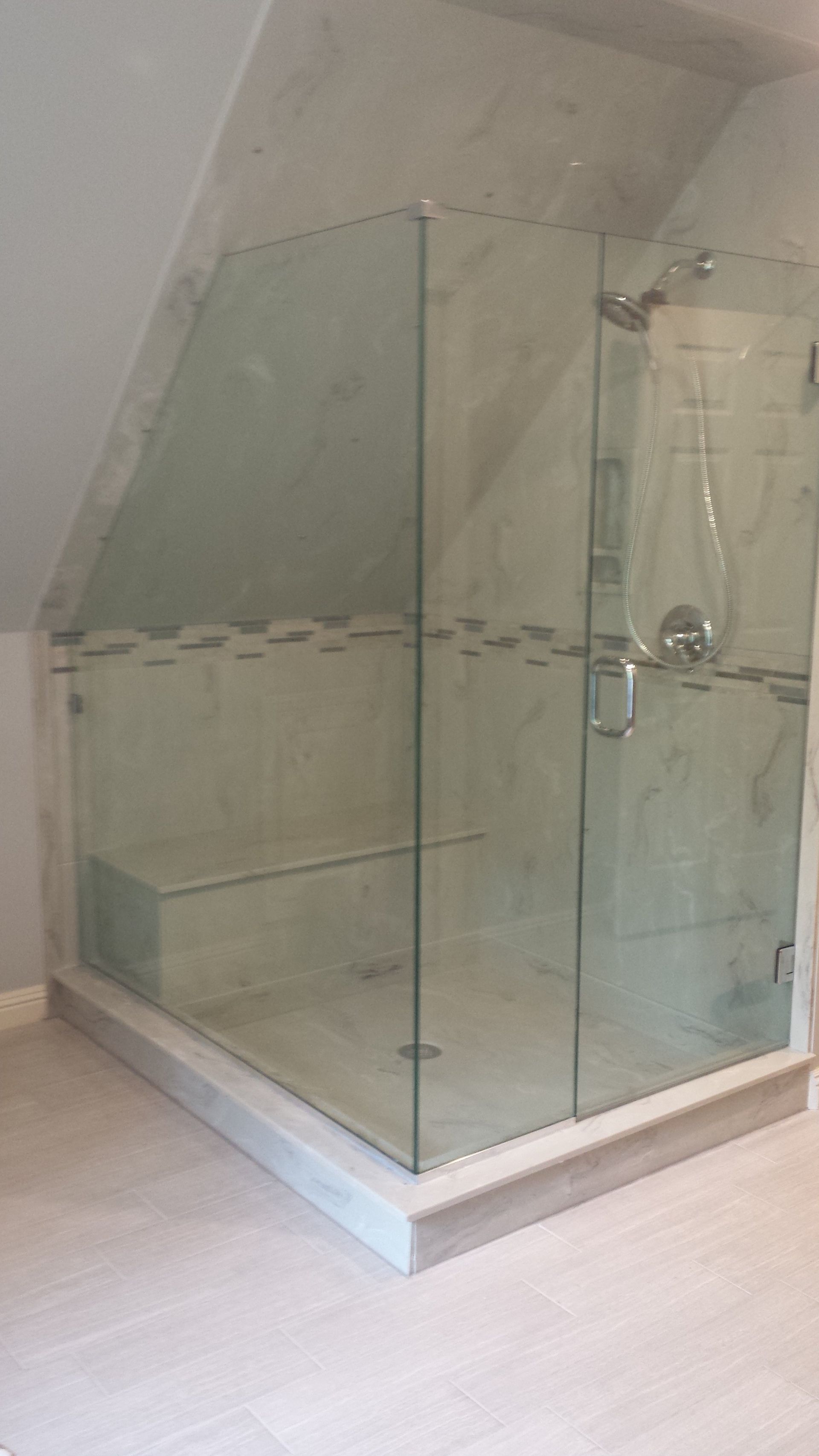 Glass shower enclosure in a bathroom with a slanted ceiling and marble-like tile.