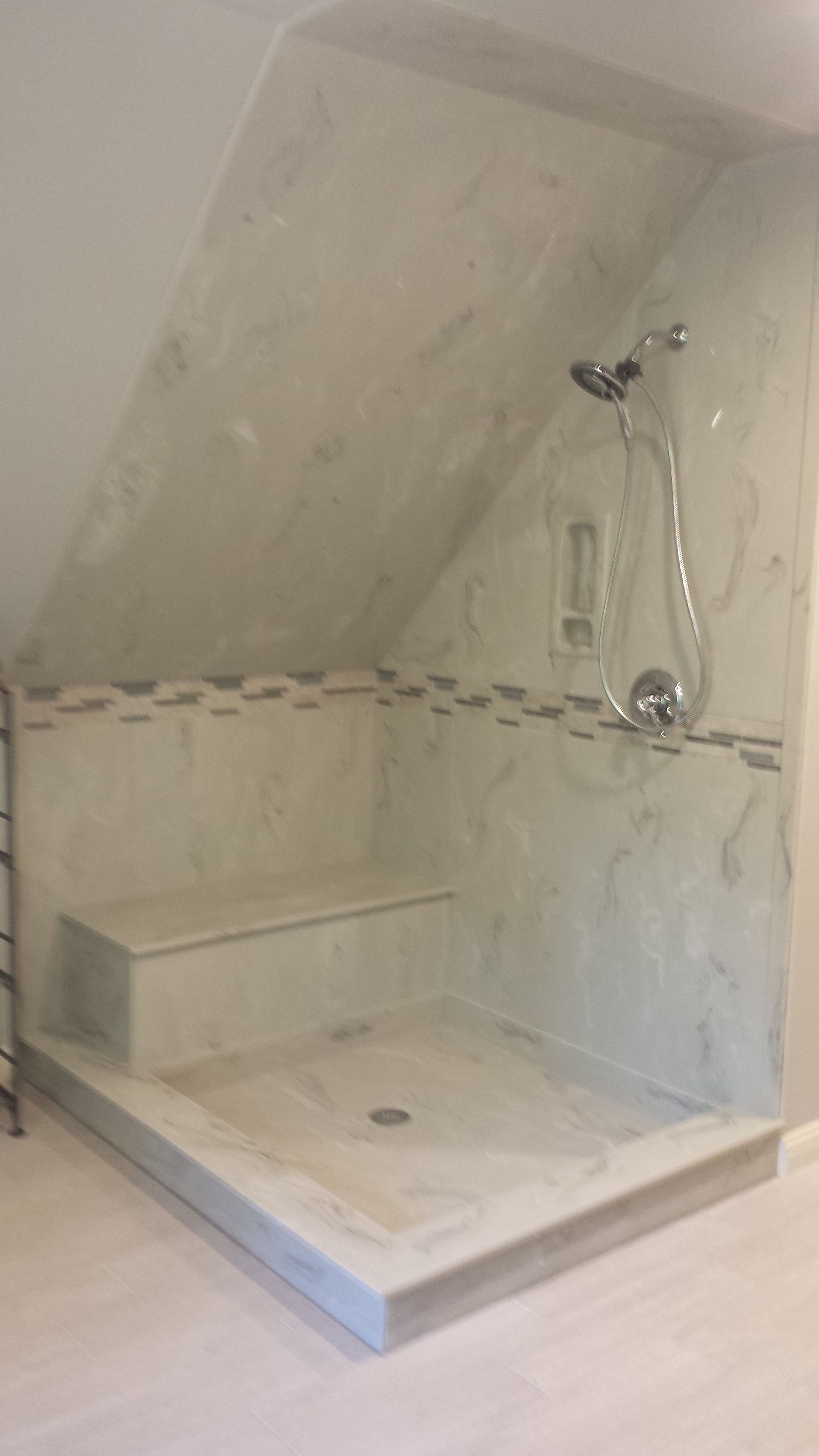 Angled shower with a built-in bench, gray and white marble-like tile, chrome shower fixtures.