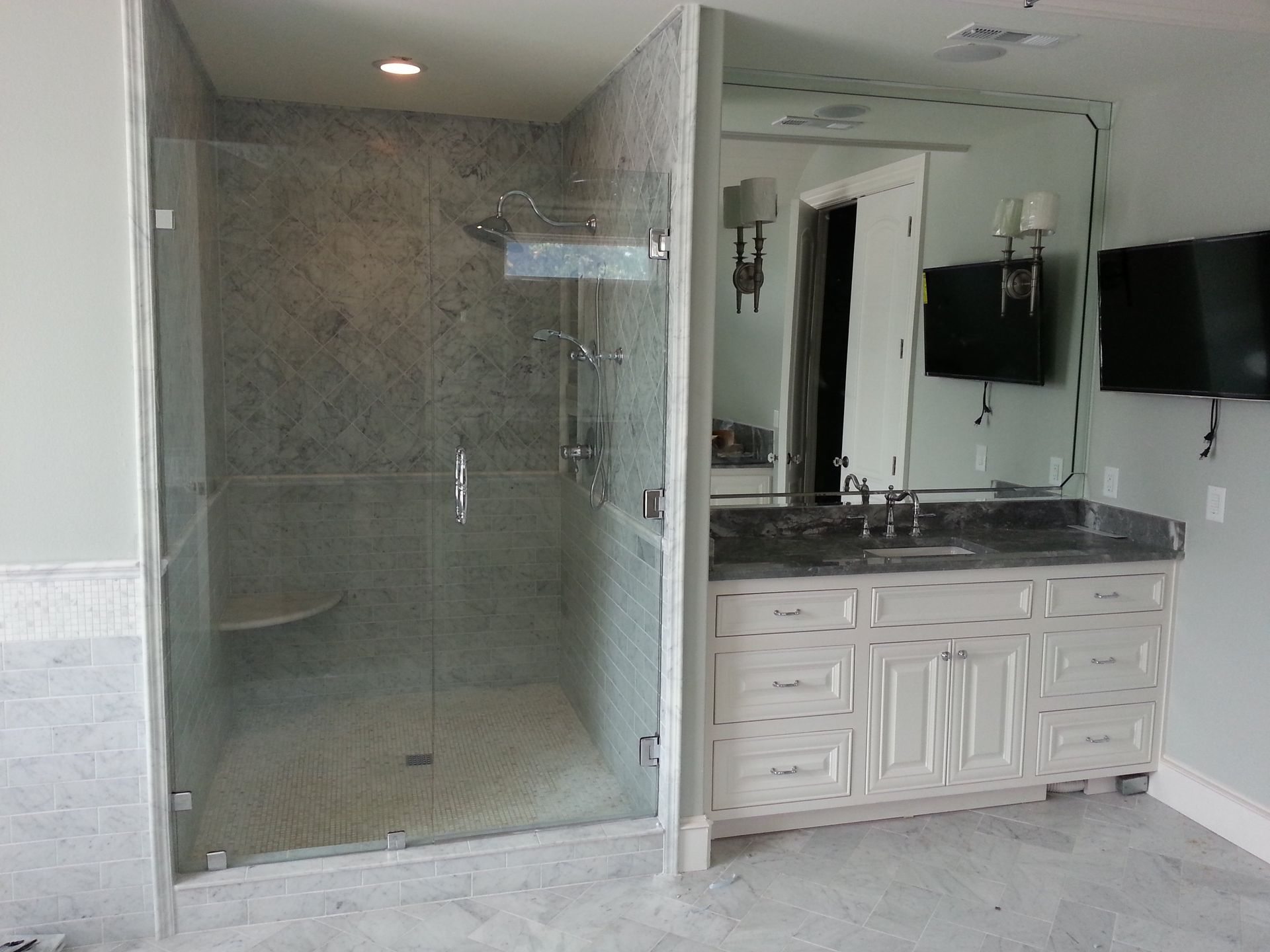A modern bathroom with a glass shower, vanity, and two wall-mounted TVs.