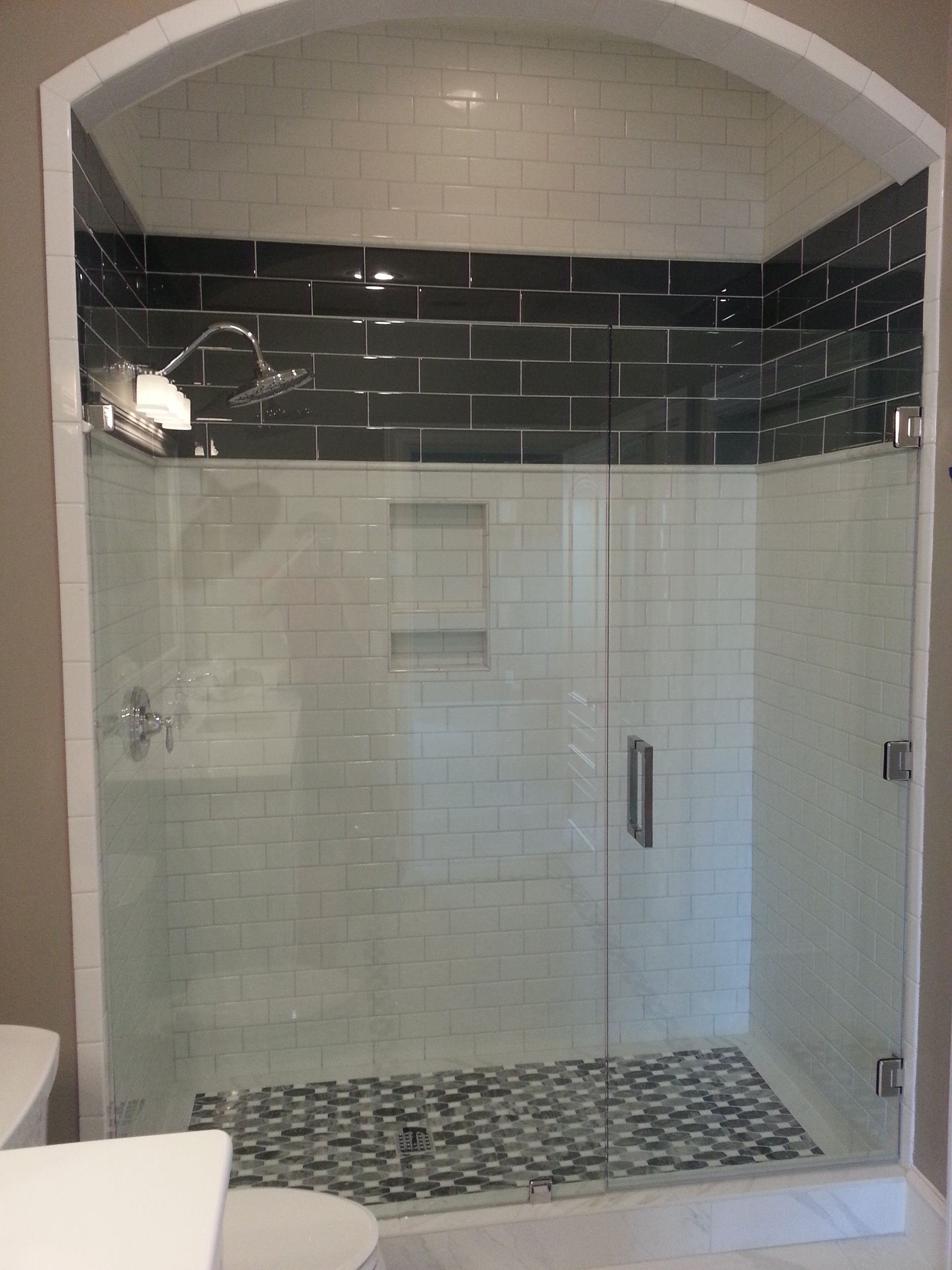 Shower with white and dark gray tile, glass door, and mosaic floor.