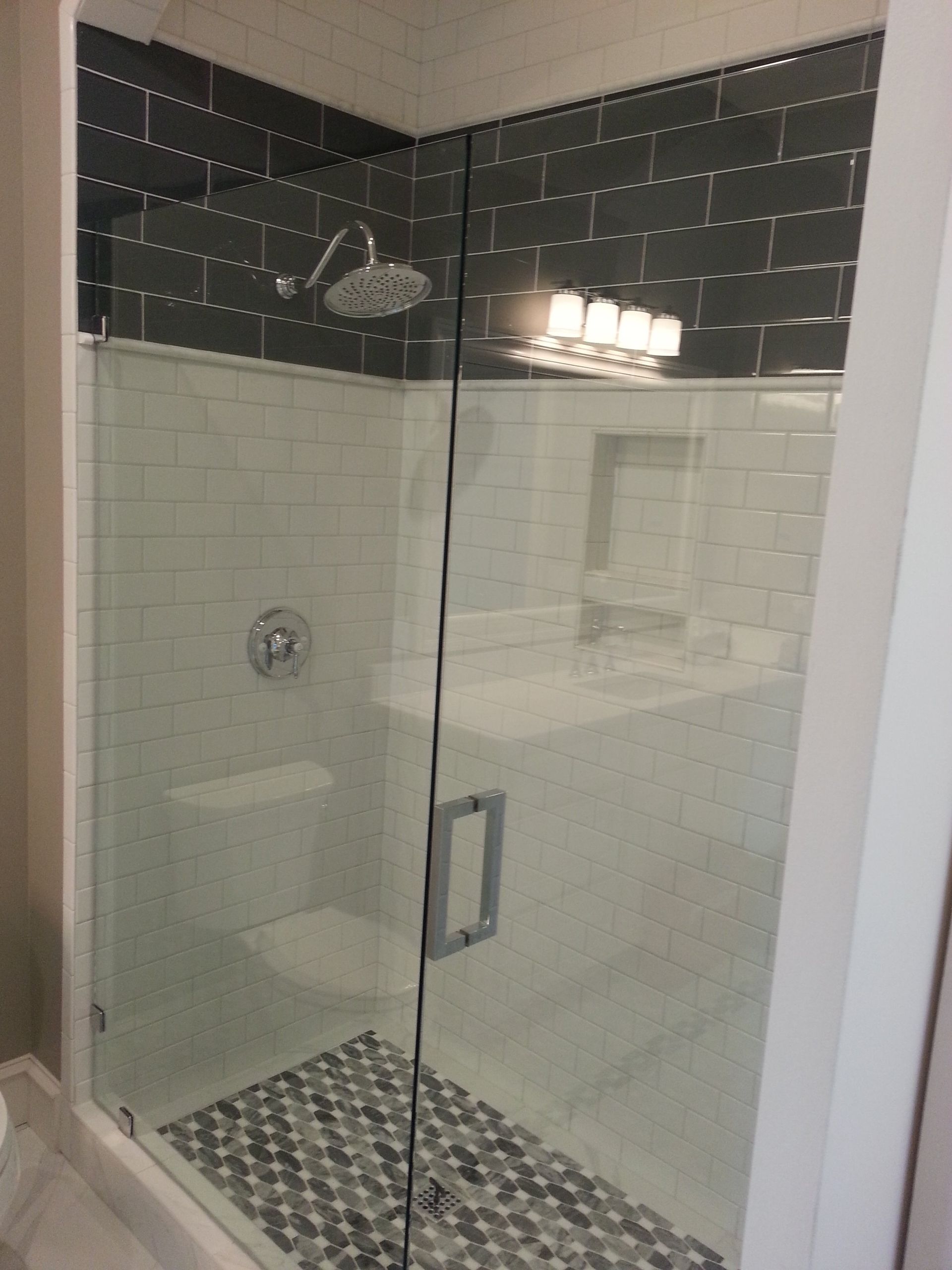 Shower with glass door, white and gray tiled walls, and a dark gray top section.