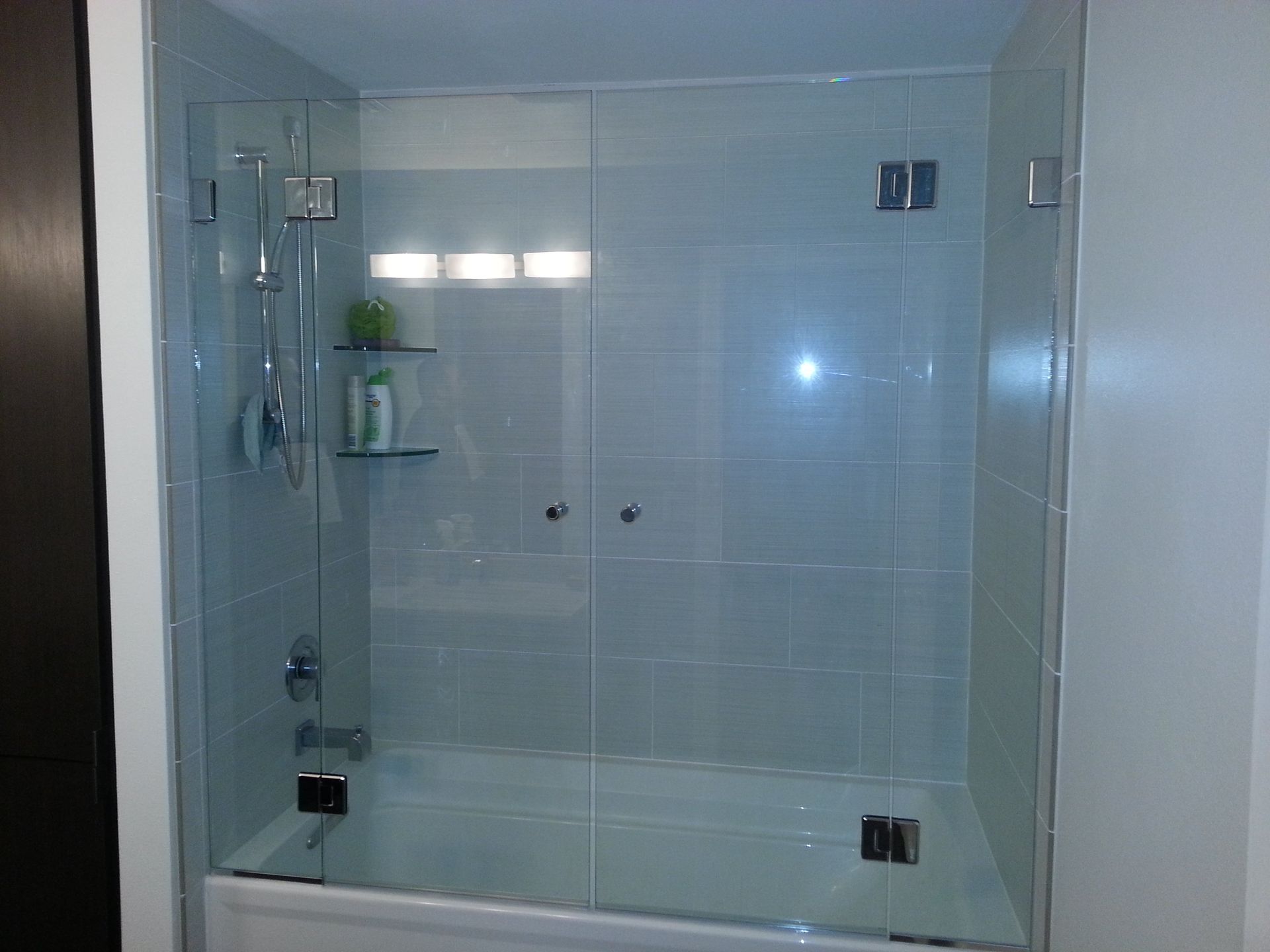 Shower stall with two clear glass doors and silver fixtures. White tile walls.
