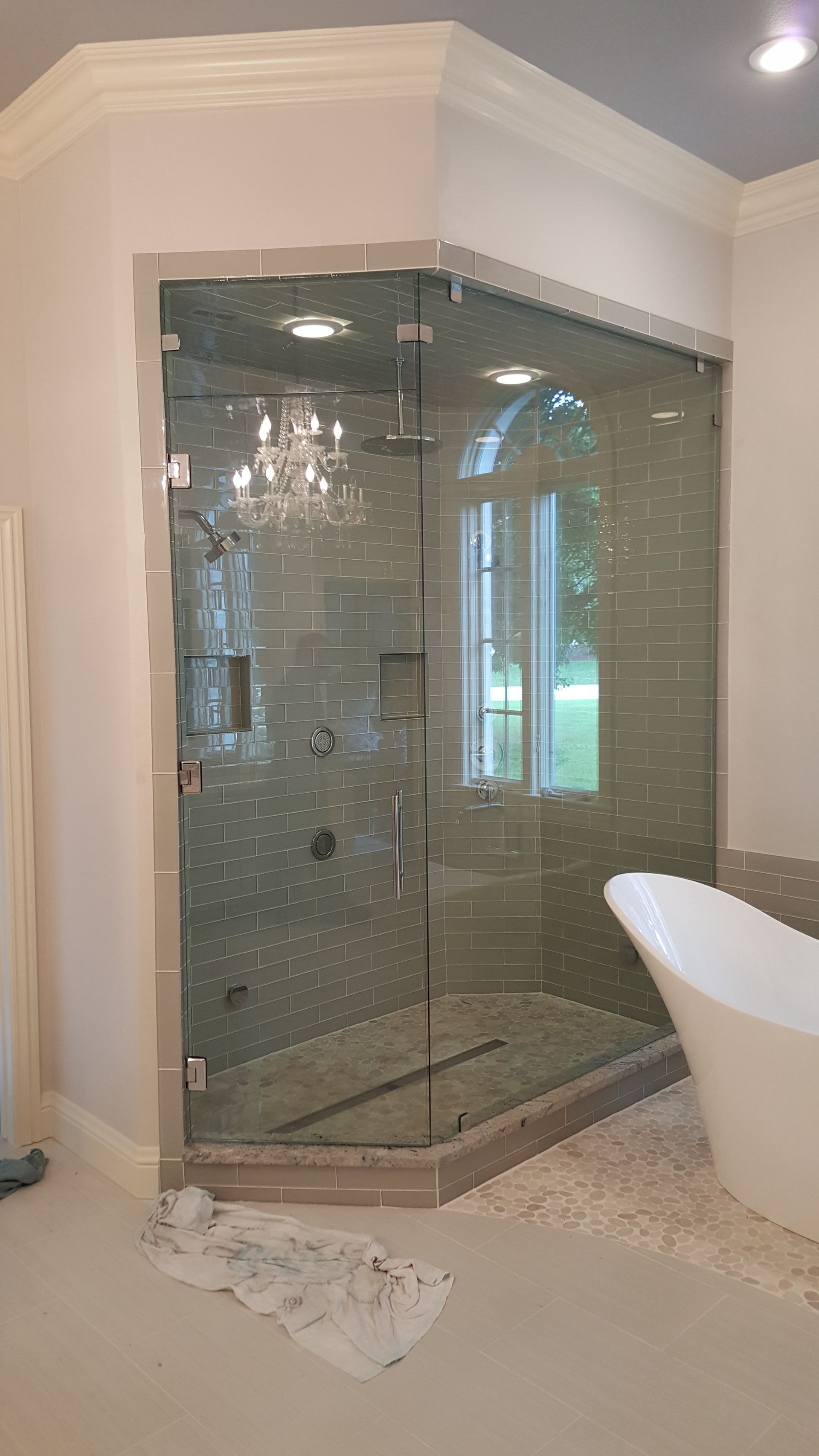 Corner shower with clear glass walls, gray tile, and white bathtub in a bathroom.