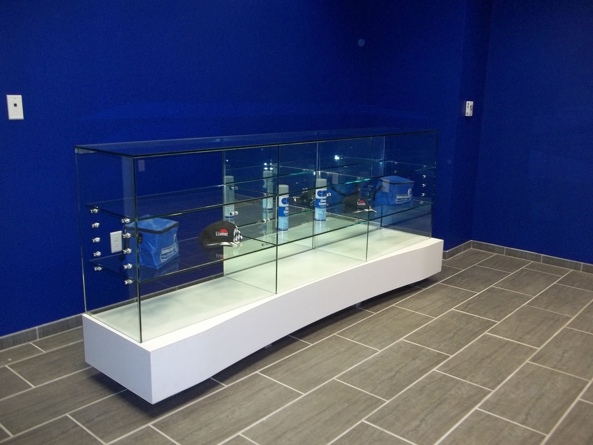 Glass display case with merchandise on a white base, set against blue walls and tiled floor.