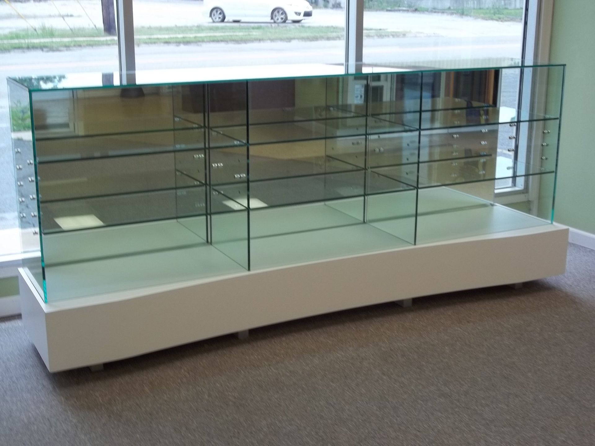 Glass display case with white base, inside a store, with reflective surfaces.