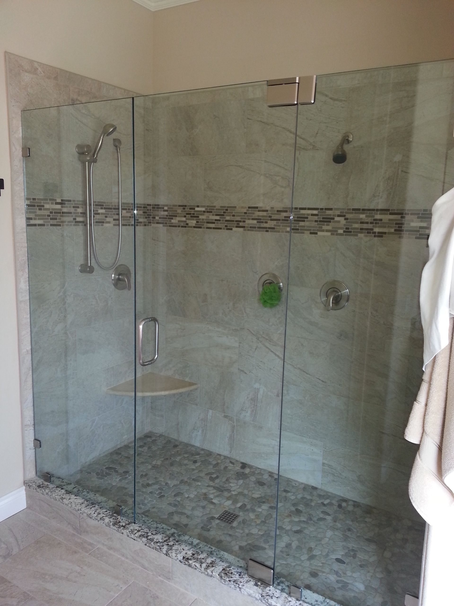 Glass shower enclosure with gray stone tile and a bench.
