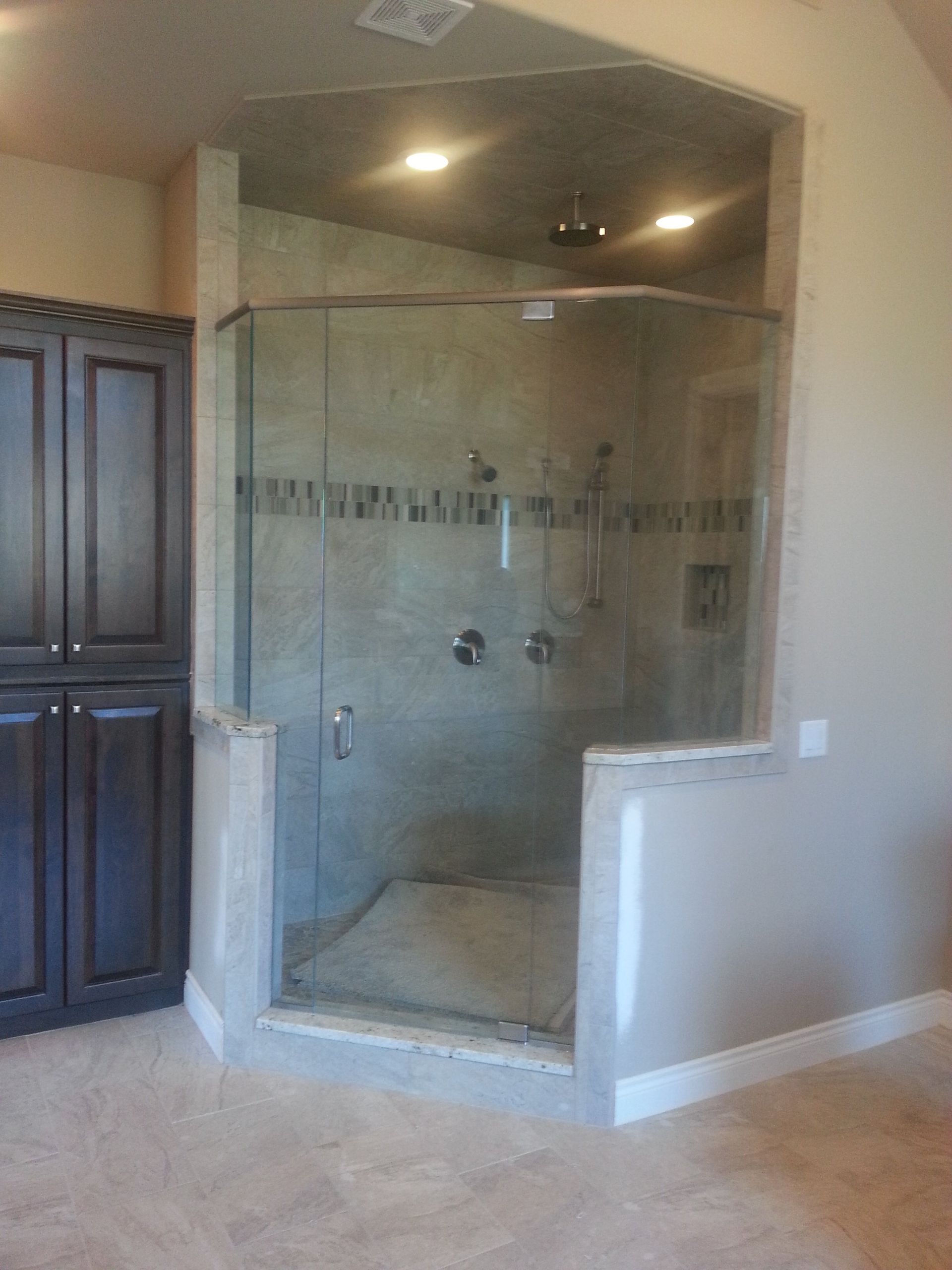 A walk-in shower with glass doors, tile walls, and a built-in bench, in a tan-colored bathroom.