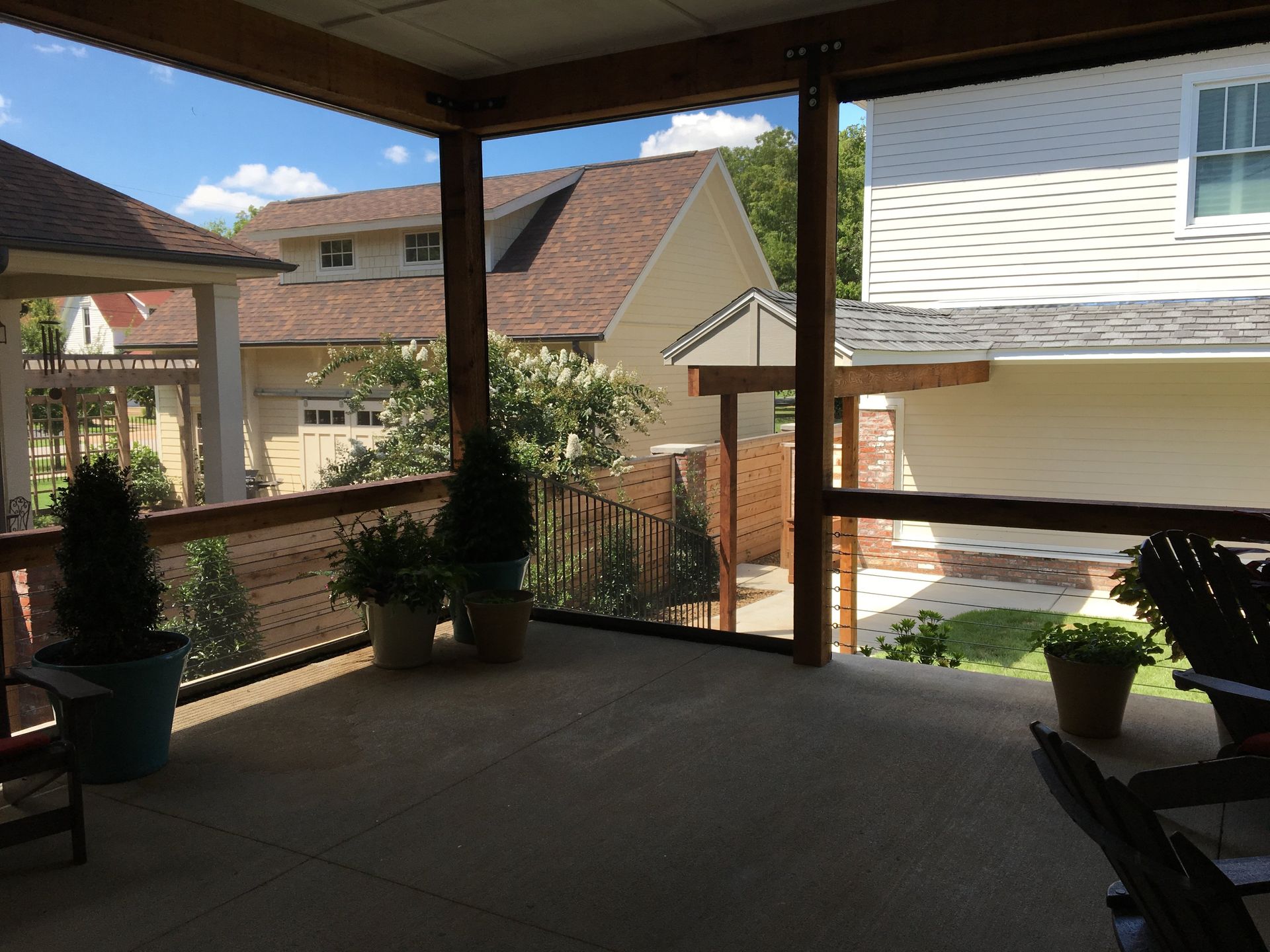 Covered porch with views of neighboring houses, potted plants, and sunny sky.