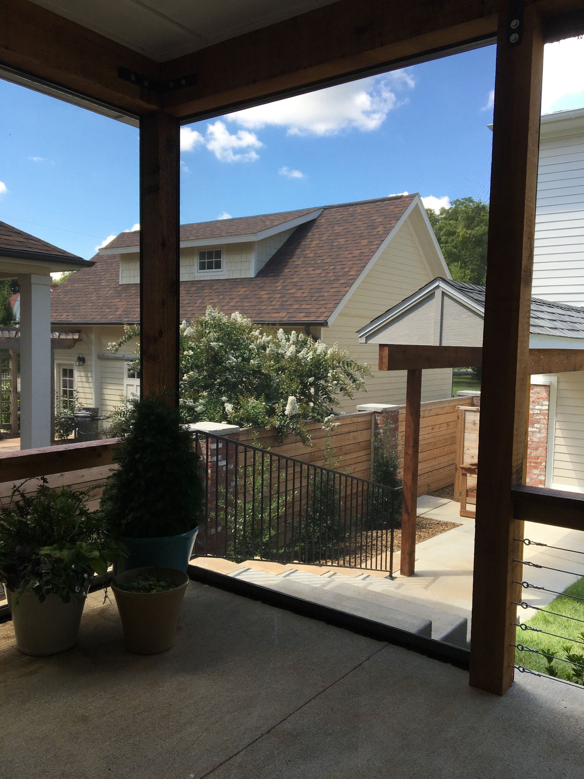 View from a screened porch overlooking a yard with houses, trees, and a blue sky.