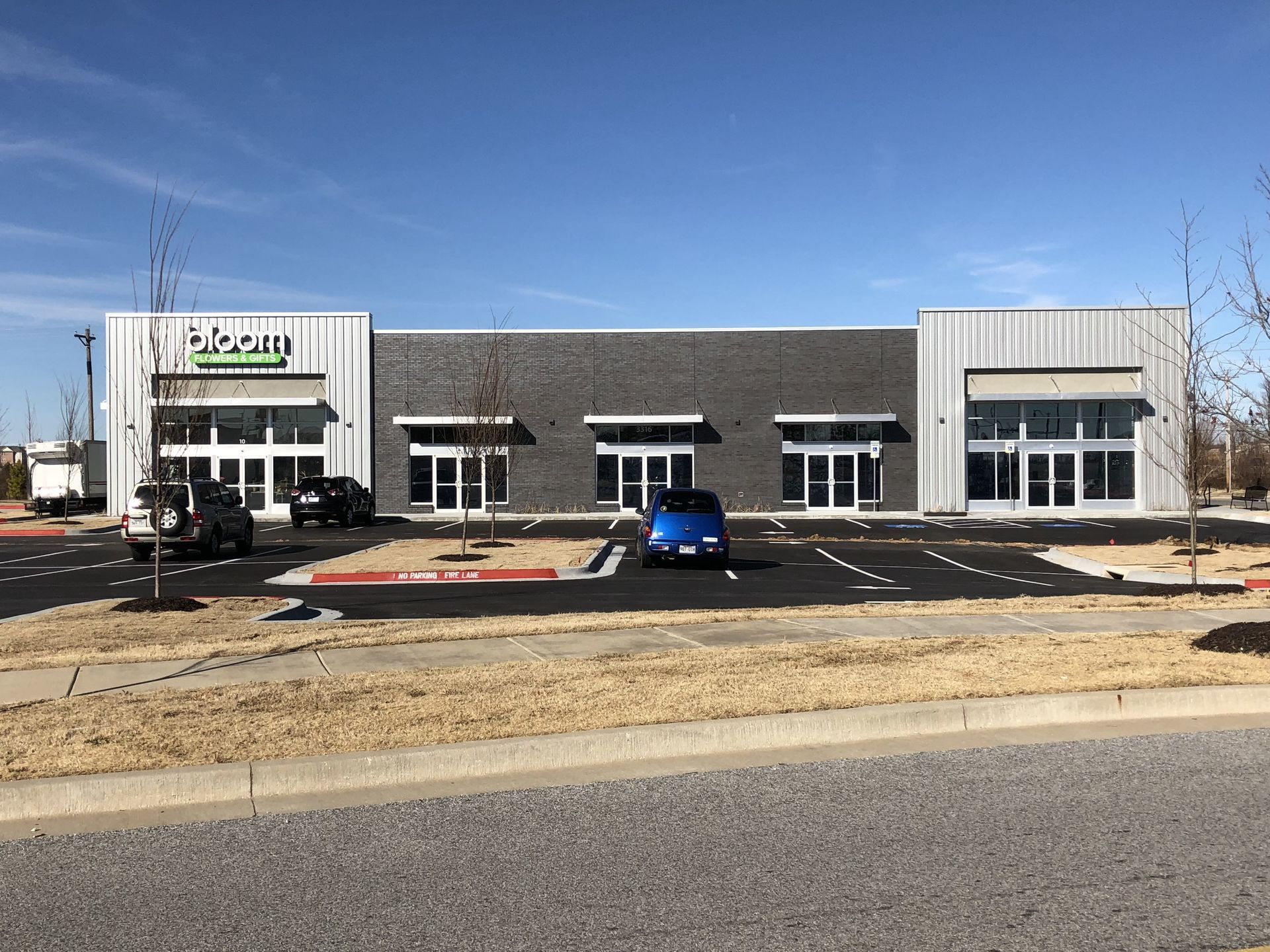 A modern building with a green sign, gray metal siding, and large glass windows. Several cars are parked in front.