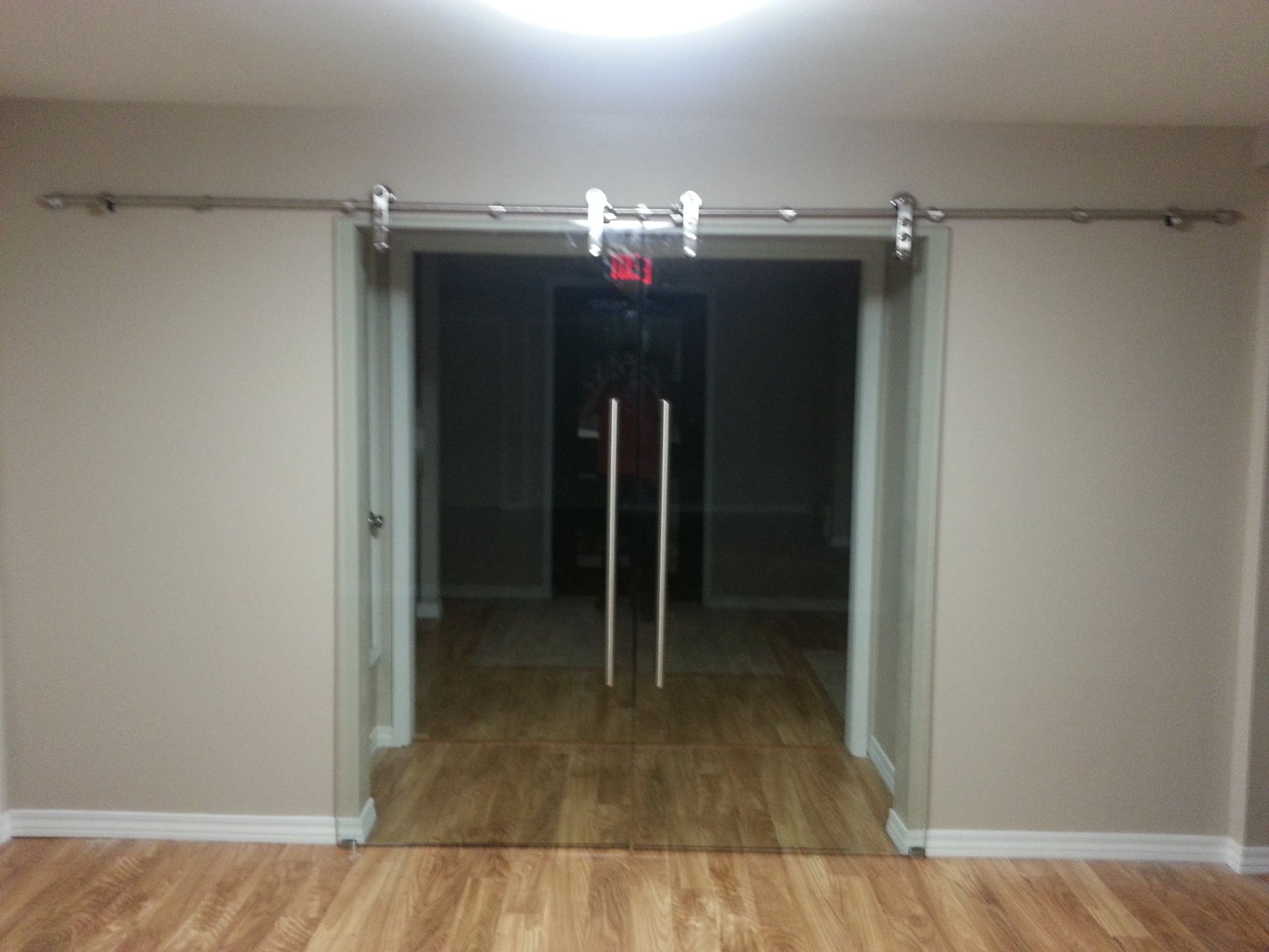 Glass sliding doors with silver hardware in a neutral room, leading to another room with wood flooring.