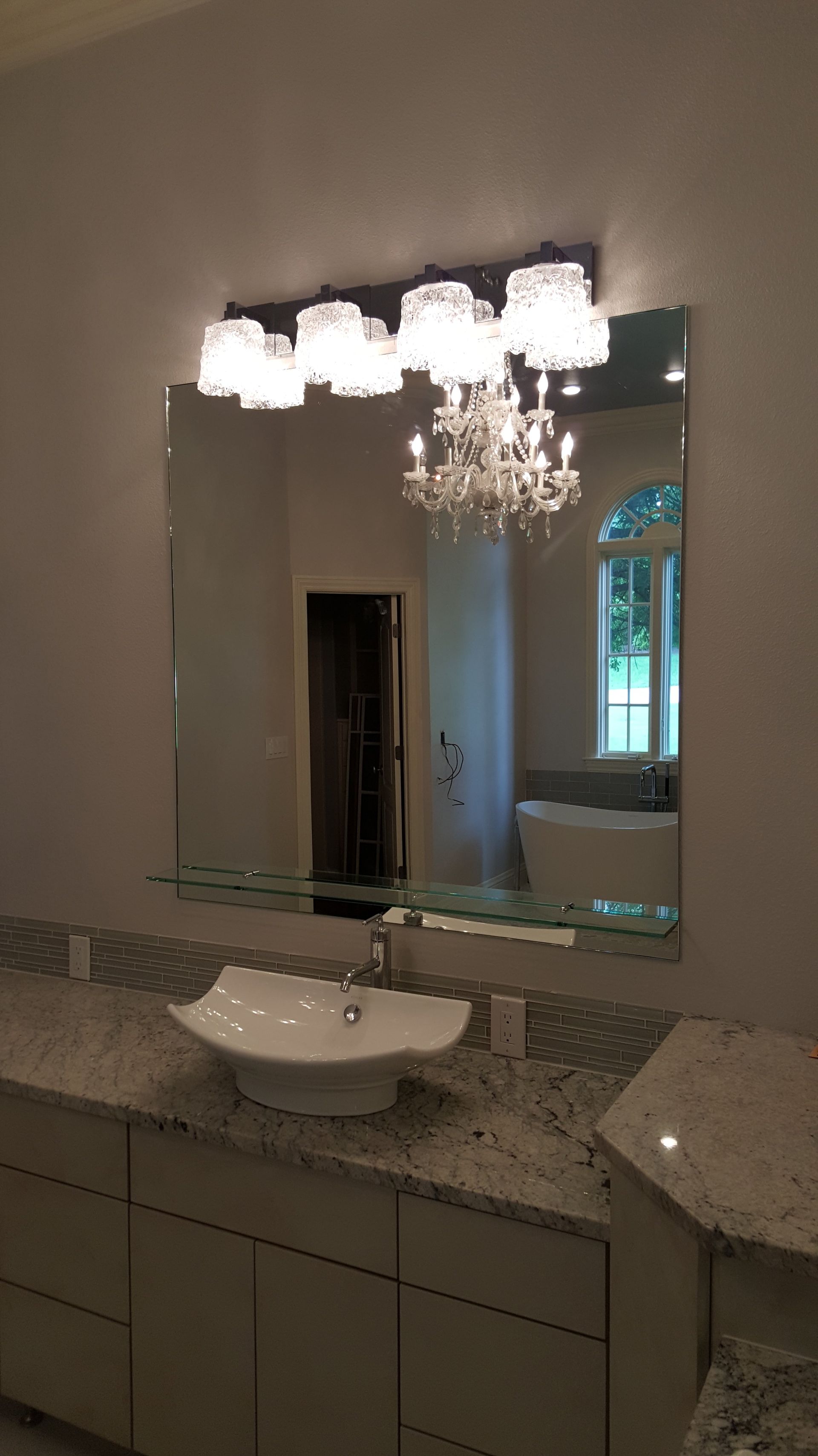 Bathroom with a white sink, gray countertop, large mirror, and chandelier reflection.