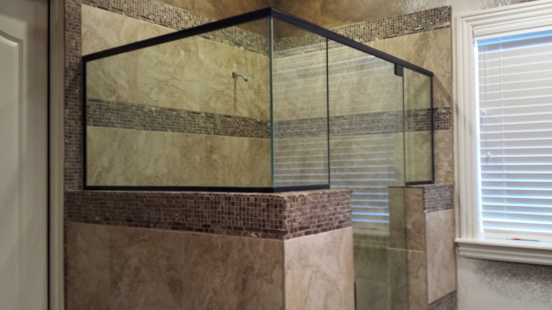 An empty glass aquarium sits atop a tiled corner structure in a room with a window.