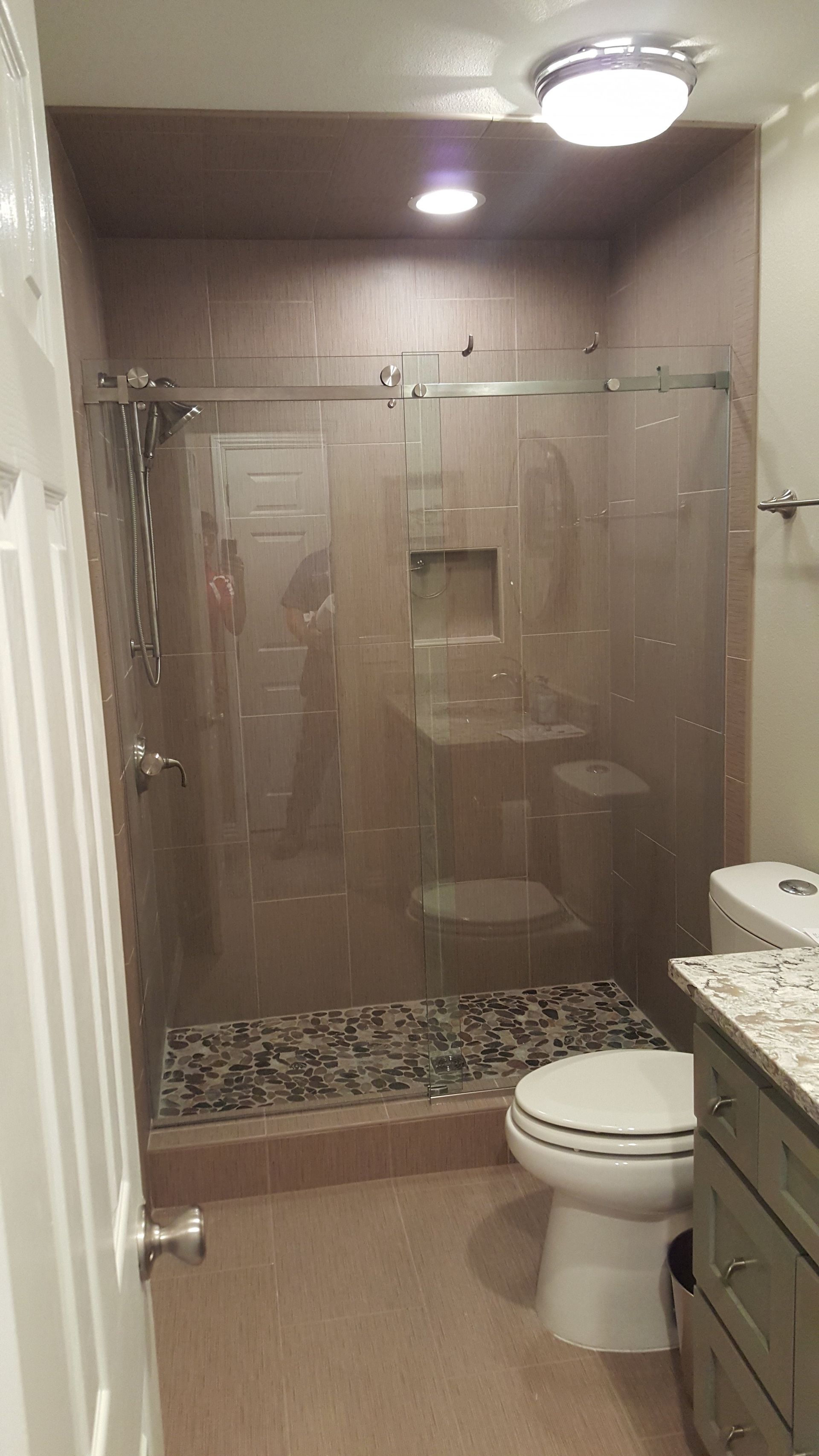 Bathroom with a stone-tiled shower, glass door, and pebble floor; next to a toilet and vanity.