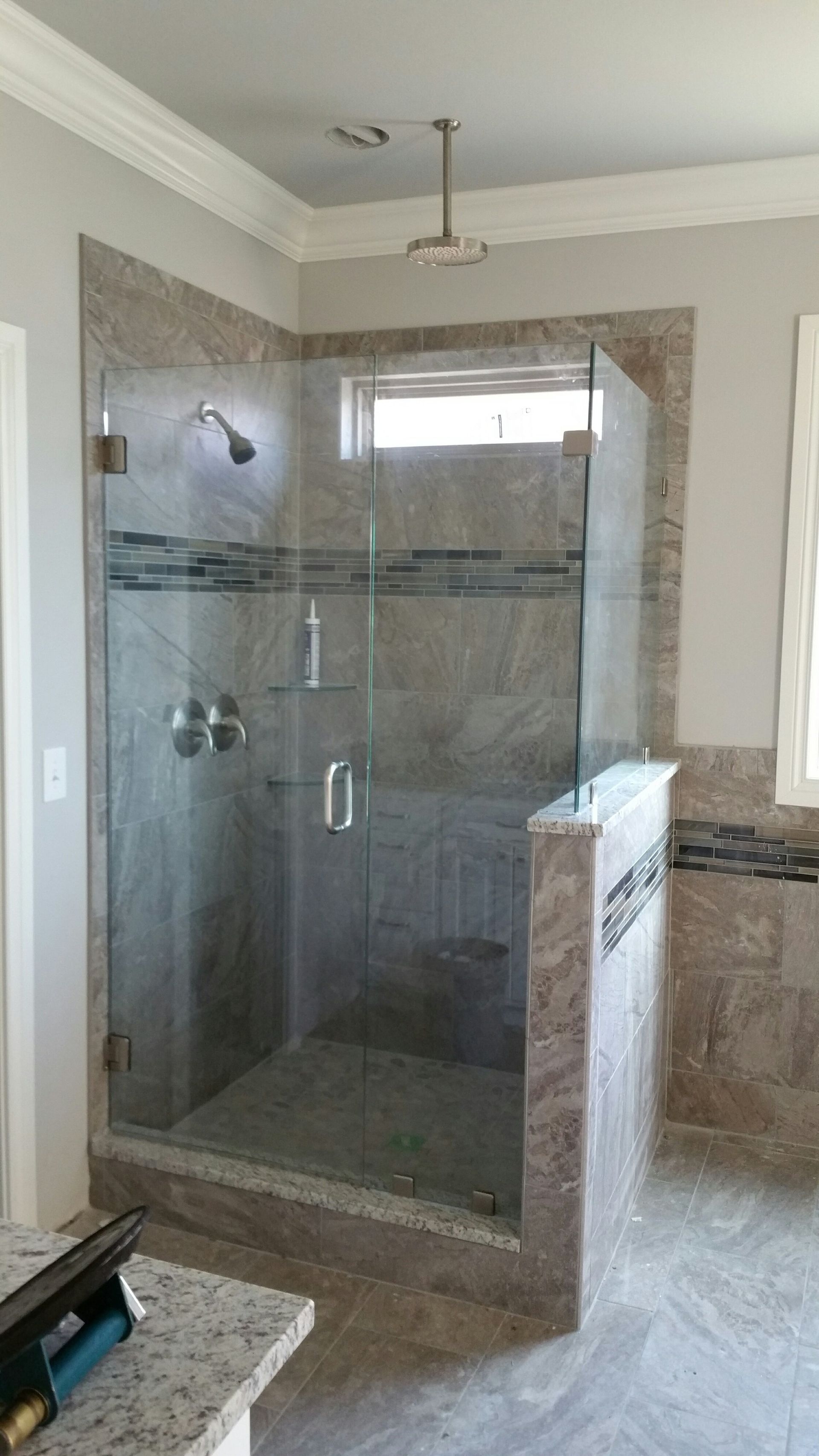 Walk-in shower with glass doors, tiled walls, and a window, in a light-colored bathroom.