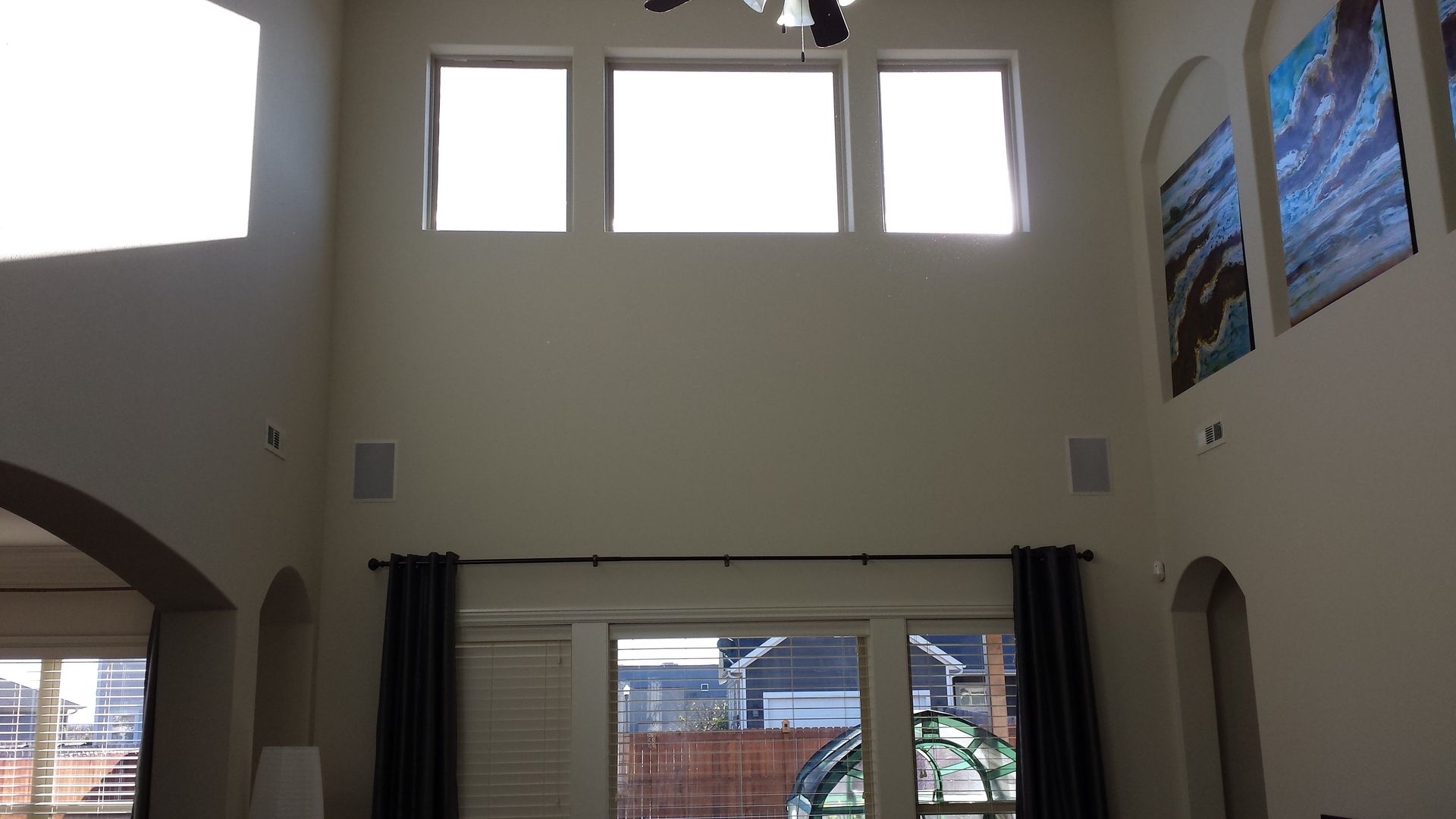 A two-story living room with tall windows and dark curtains, bright light.
