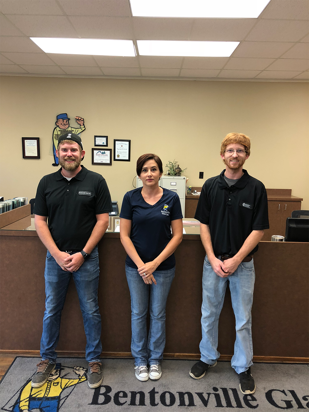 Three employees standing behind a counter in an office; two men and one woman.