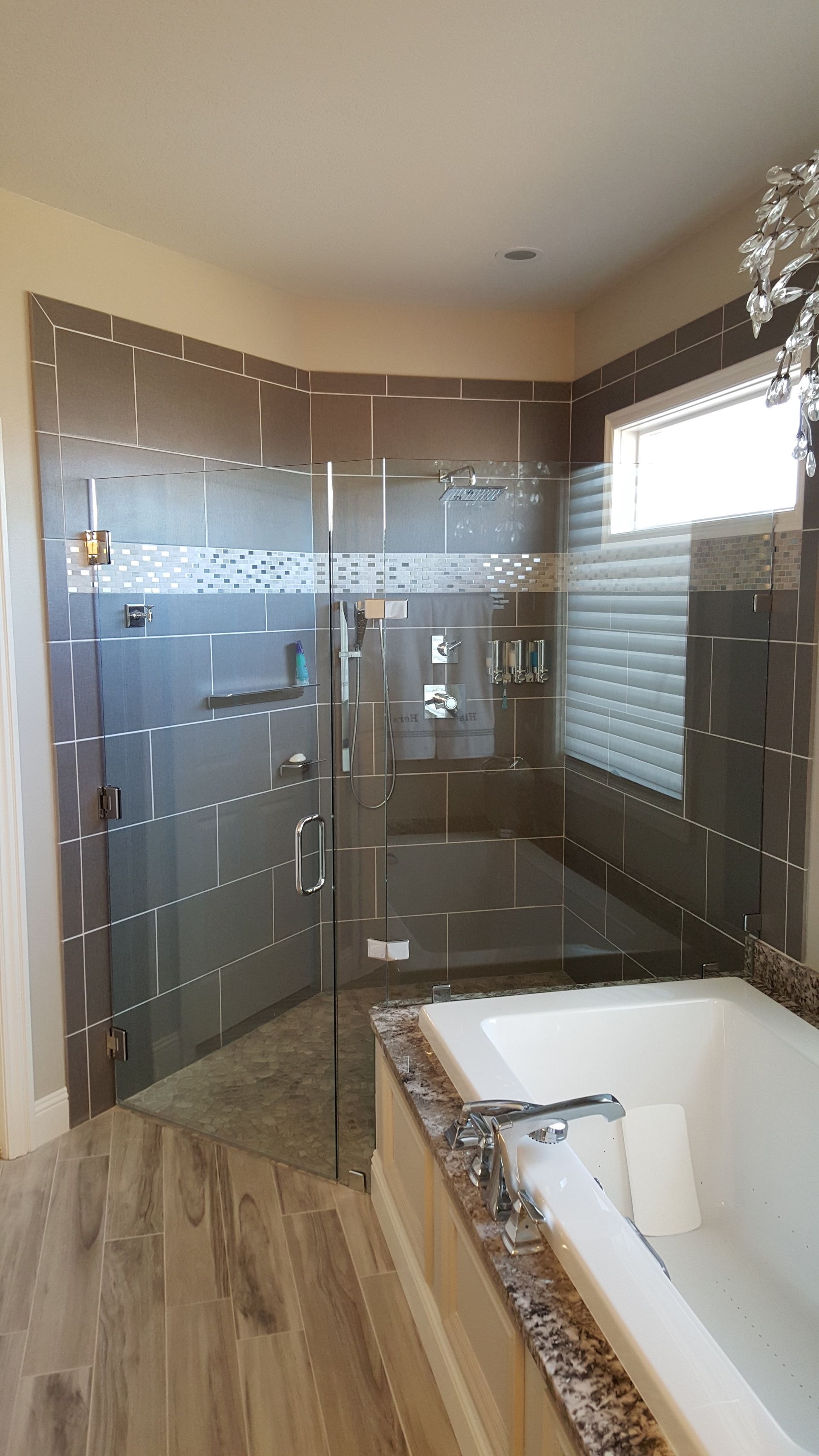 Bathroom with tiled shower, glass doors, and a bathtub. Brown and grey tiles.