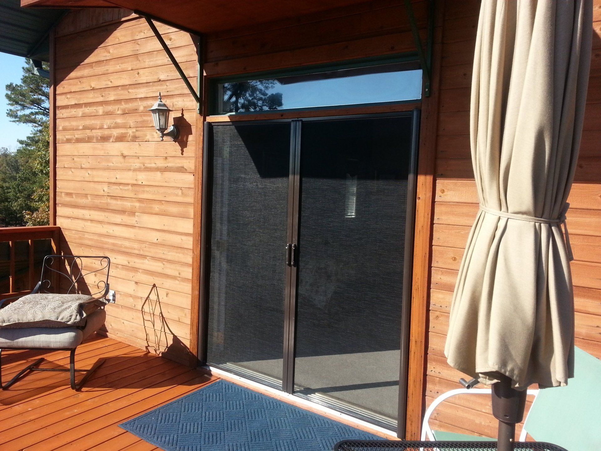 Sliding glass door with a screen on a wooden deck, next to a patio umbrella.