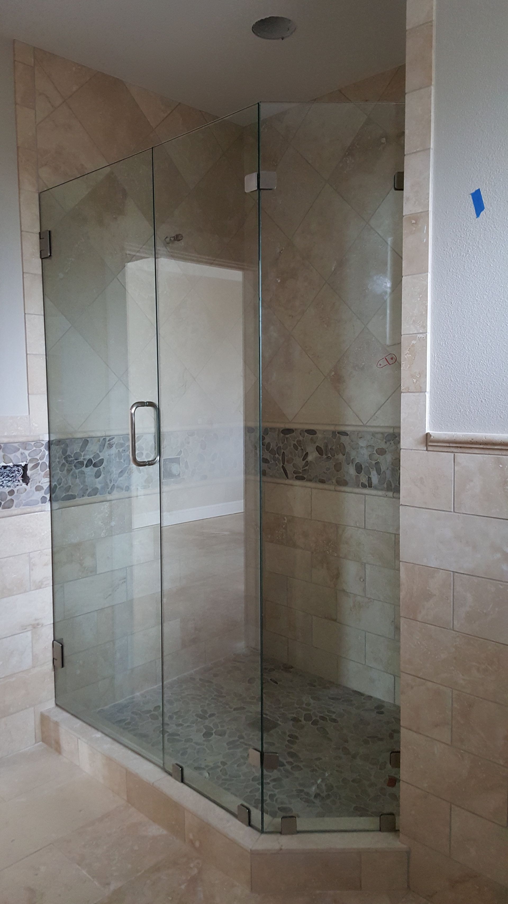 Glass shower enclosure with gray stone tile floor, beige tile walls, and a blue accent strip.