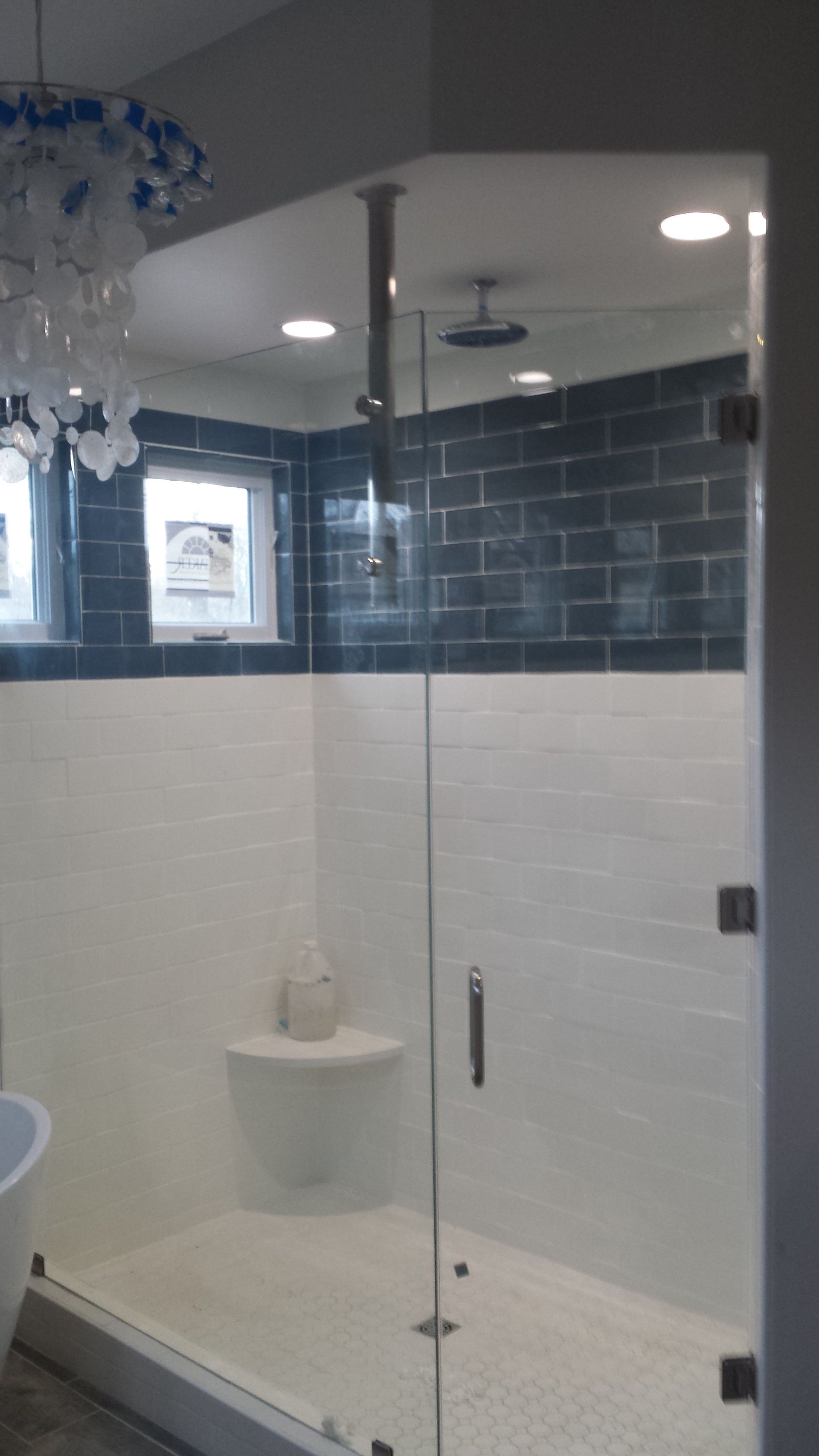 A modern shower with white and blue tile, glass door, and chrome fixtures.