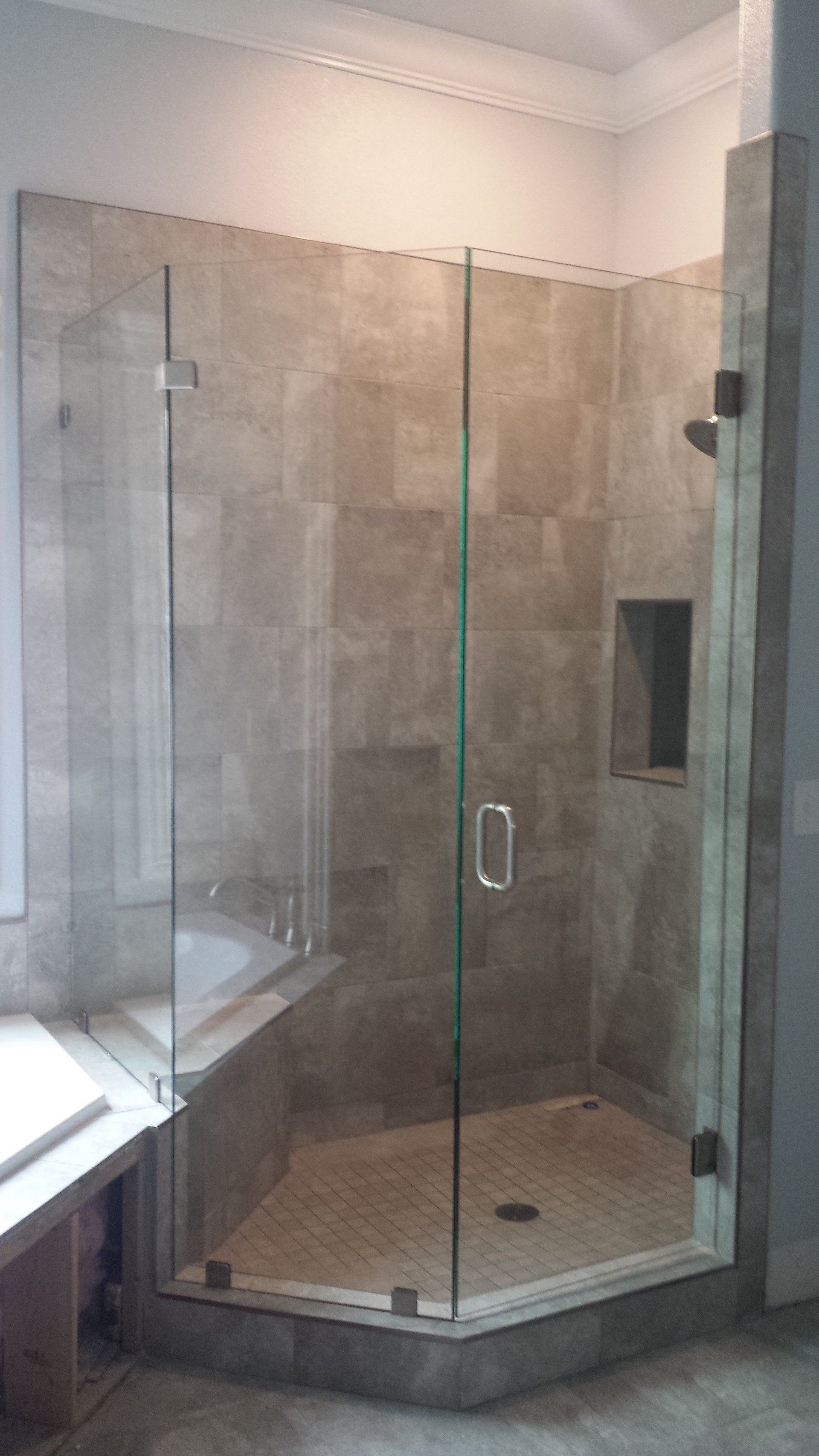 Frameless glass shower enclosure with tan tile walls and floor, small recessed shelf.