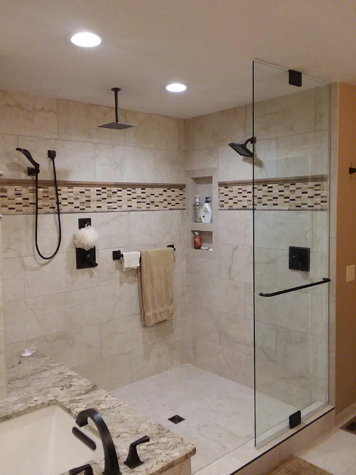 Walk-in shower with glass door, beige tile, and black fixtures. Beige and brown mosaic tile border.