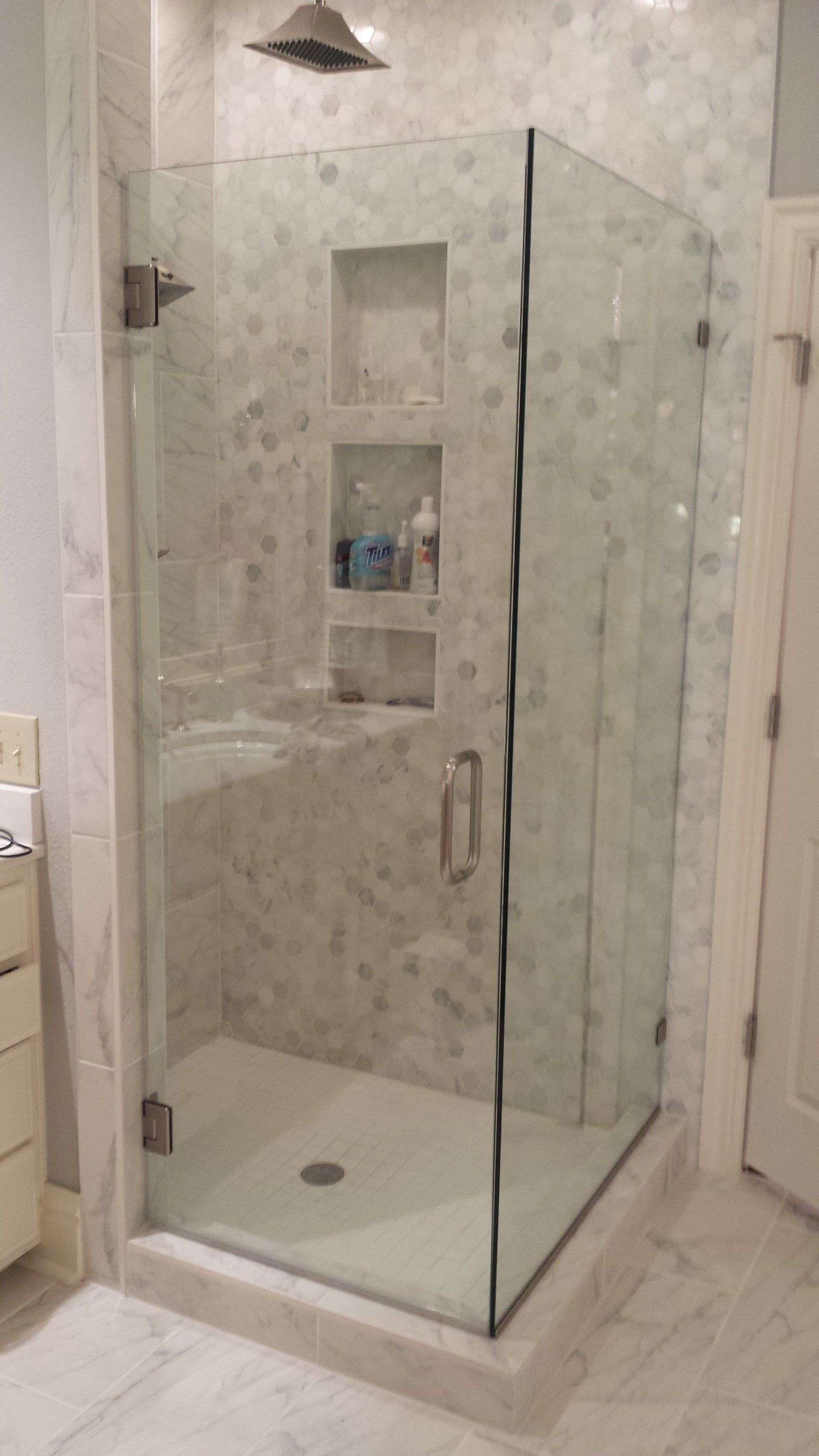 Glass shower enclosure with white tile walls, built-in shelves, and a white base.
