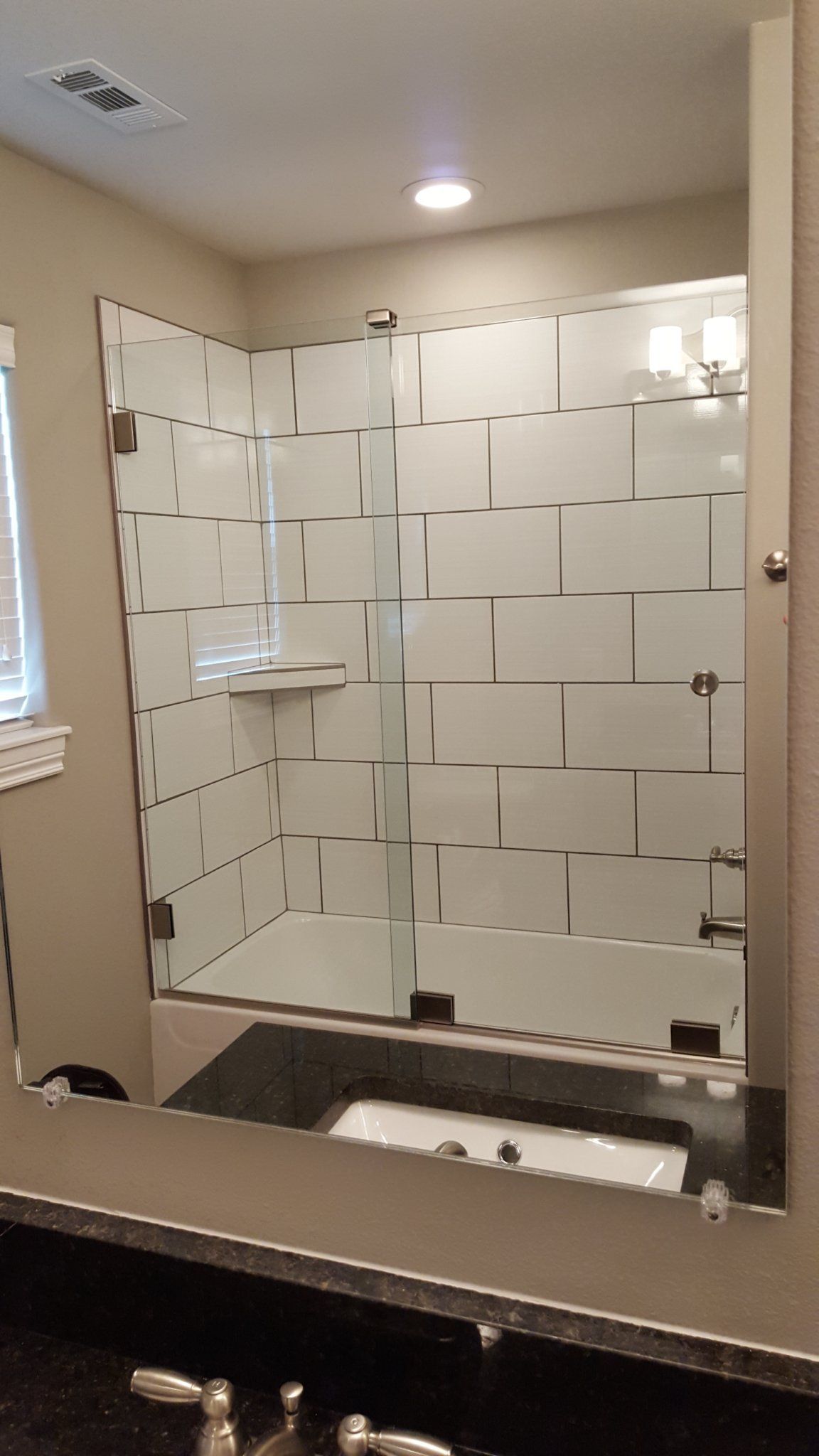 Bathroom with a mirror, shower, and sink. White tiled shower enclosure with glass doors.