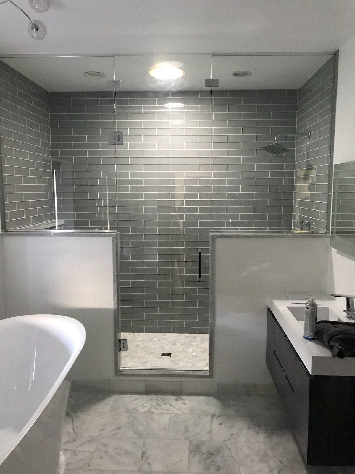 Modern bathroom with glass shower, gray-tiled walls, white accents, and a freestanding tub.