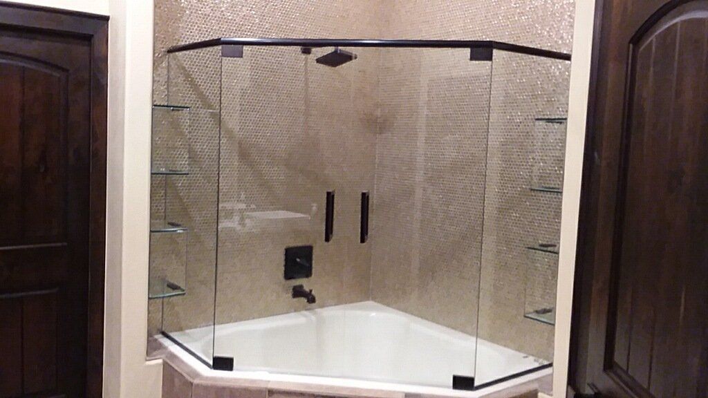Shower enclosure with glass panels, dark trim, and shelves. Bathroom with brown wood and beige tiles.